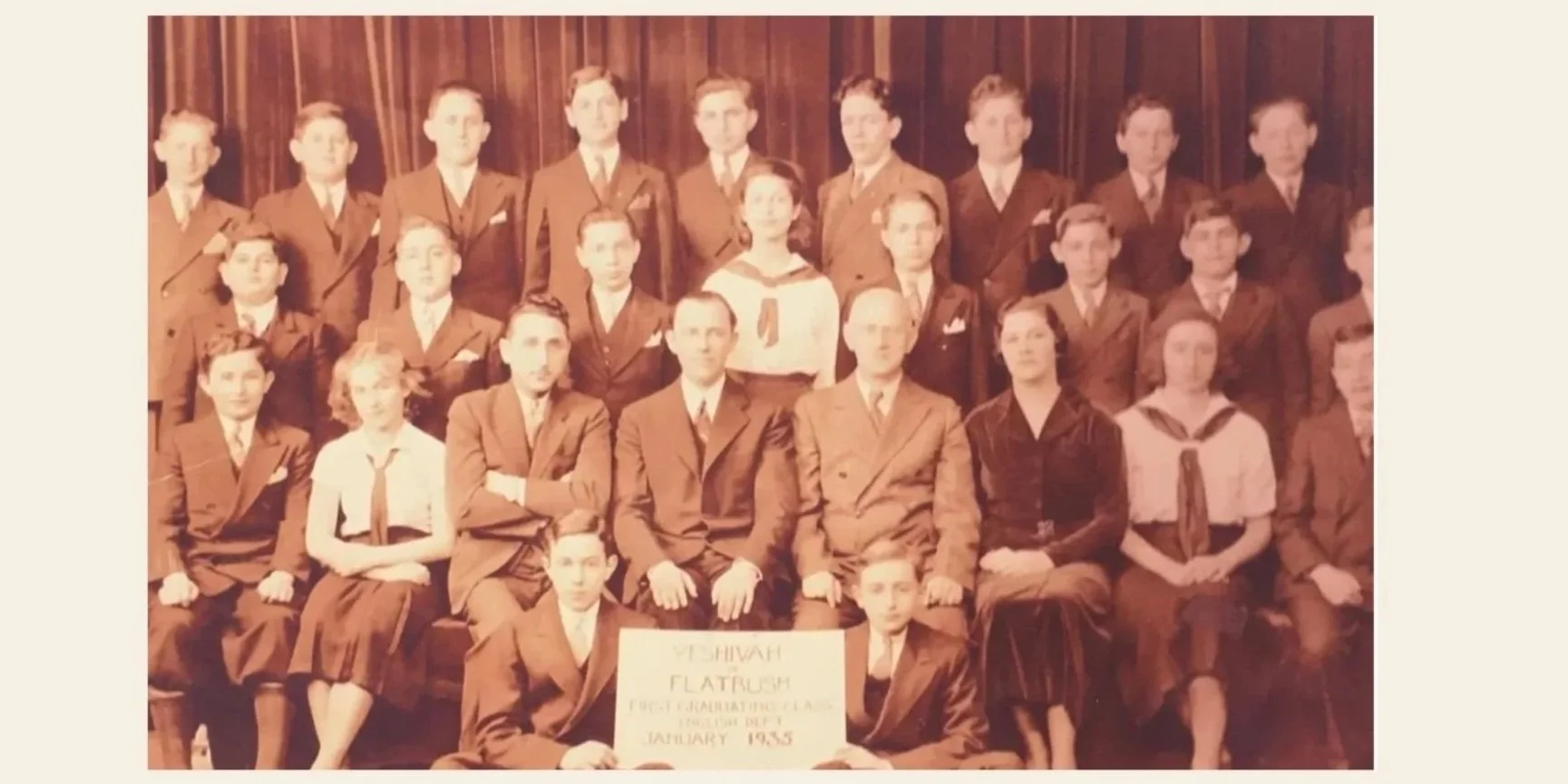 Black and white photograph of a group of students in formal uniforms, standing and sitting in front of a wooden wall. Two students in the front row hold a sign that reads 'VISHVAH FLAT RUSH, FOR GRADUATING CLASS, JANUARY 1935'.