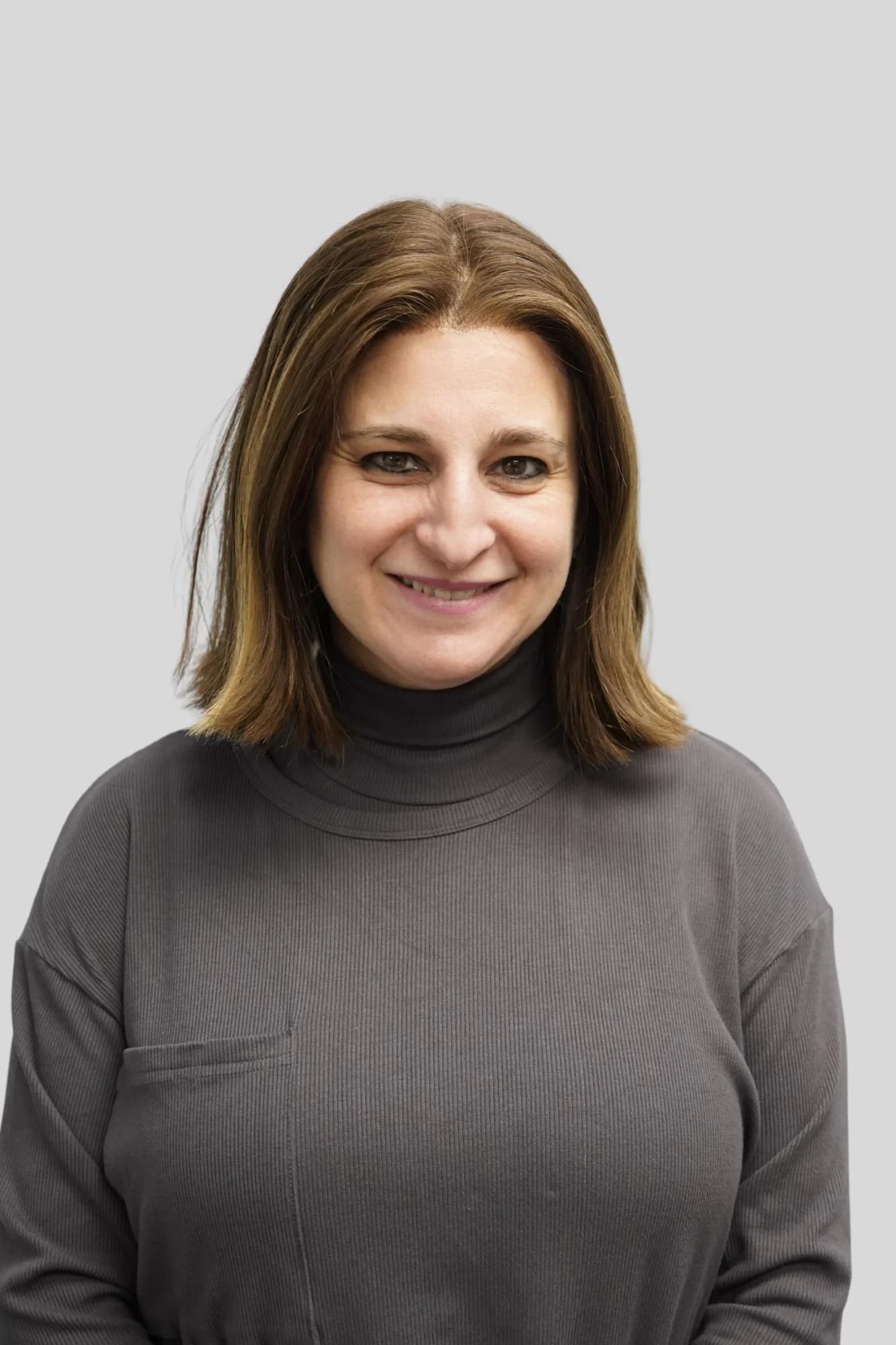 A woman with shoulder-length light brown hair, wearing a dark turtleneck sweater, smiling against a plain light gray background.