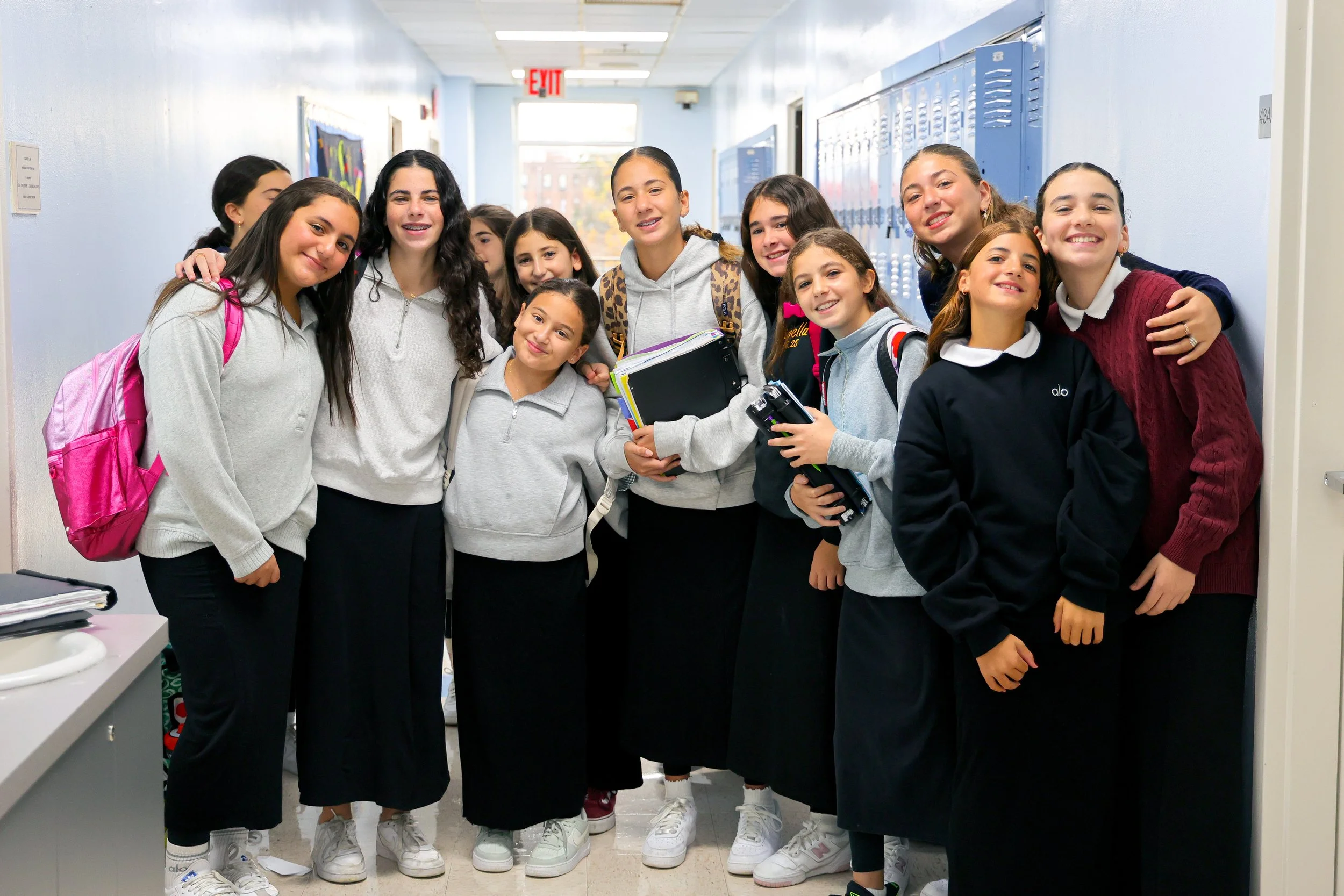 Group of diverse middle school girls smiling and posing in school hallway with blue lockers.