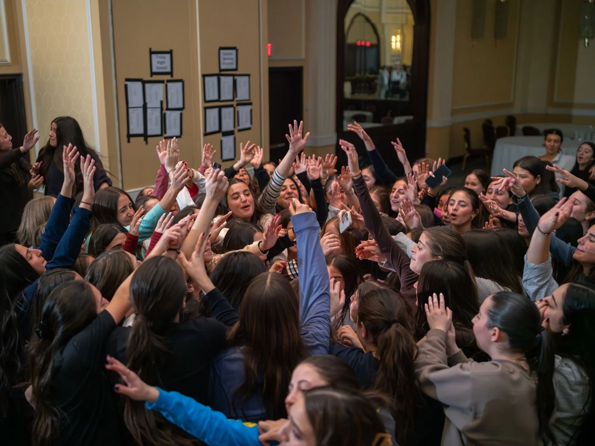 Crowd of excited young women reaching up and smiling at an indoor event.