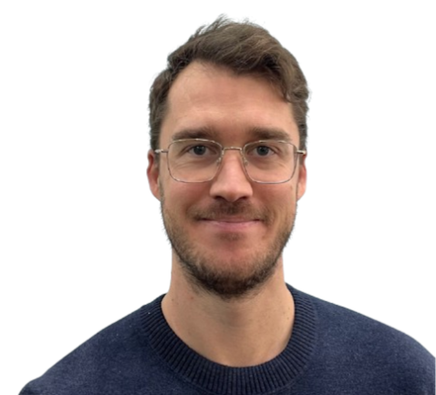 A young man with glasses and facial hair smiling at the camera, wearing a dark blue sweater.