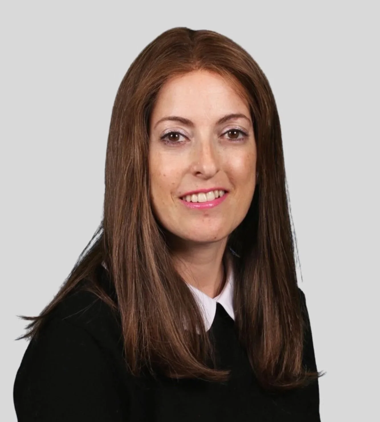A woman with long brown hair, smiling, wearing a black top with a white collar, posing against a plain gray background.