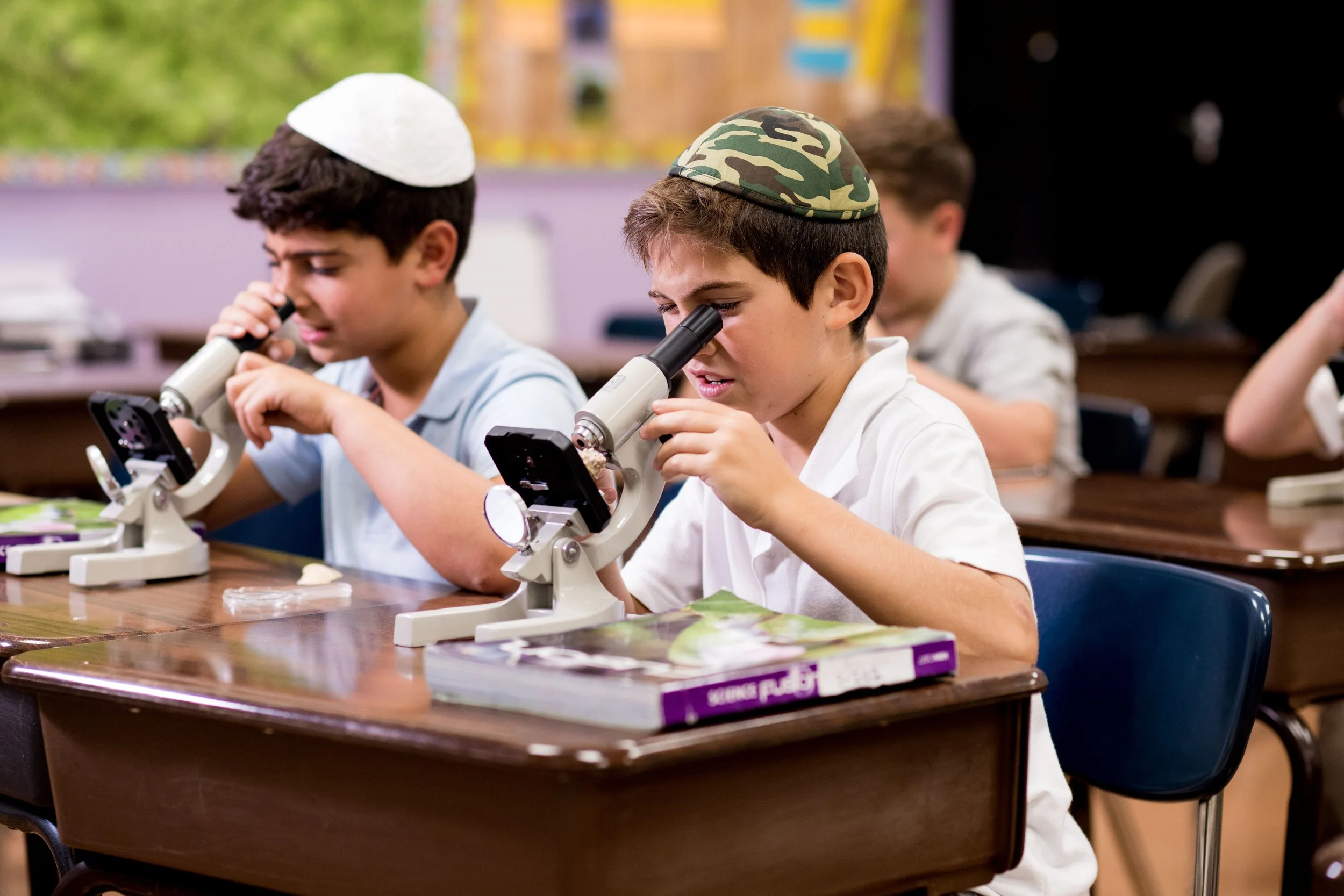 Young boys wearing yarmulkes looking into microscopes in a classroom.