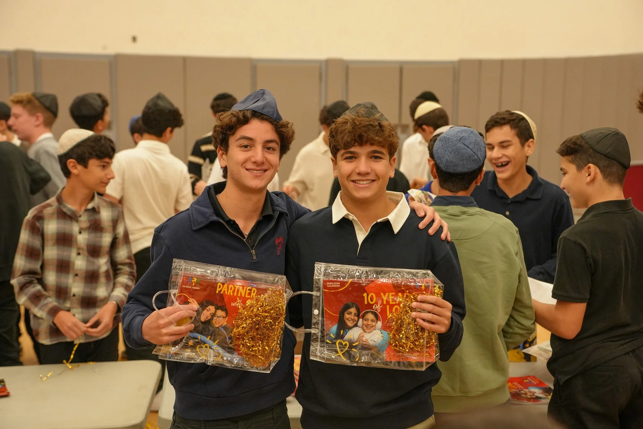 Two teenage boys smiling and holding acknowledgment plaques at a crowded event with many other boys in the background.