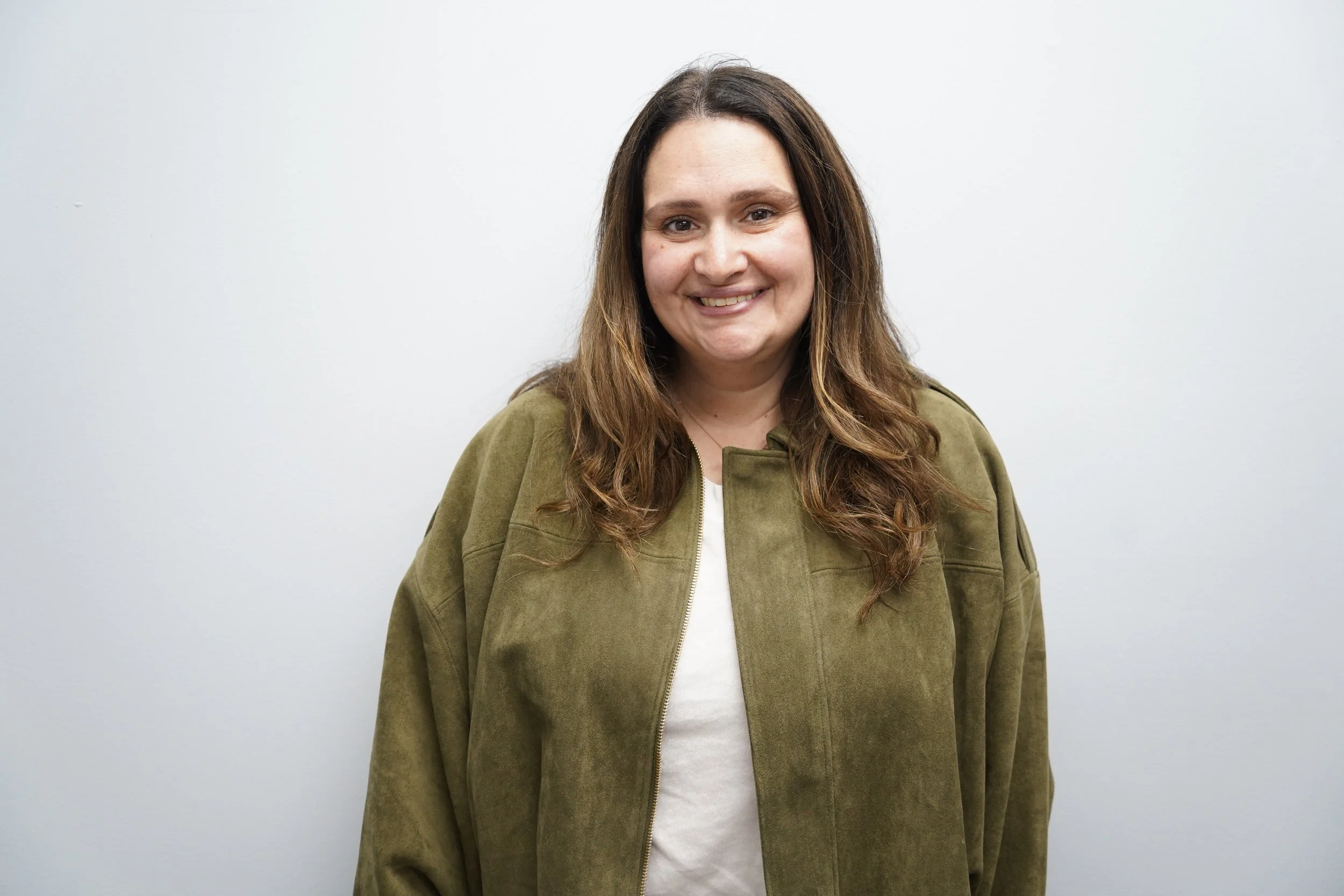 A woman with brown hair wearing a green jacket and white shirt, standing against a plain white background.