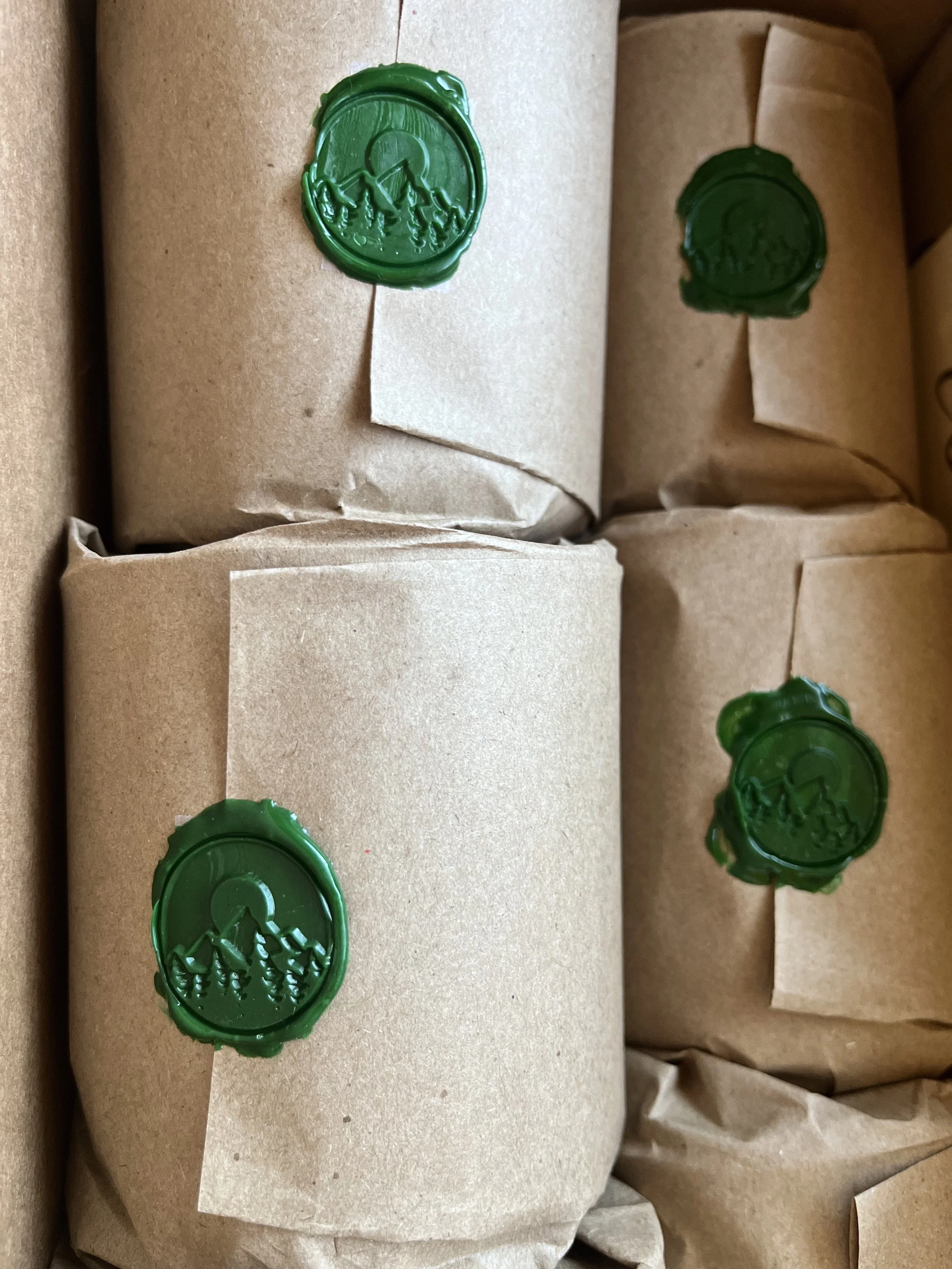 Several packages wrapped in brown paper with green wax seals stamped with a Cascade Mountain and tree design.
