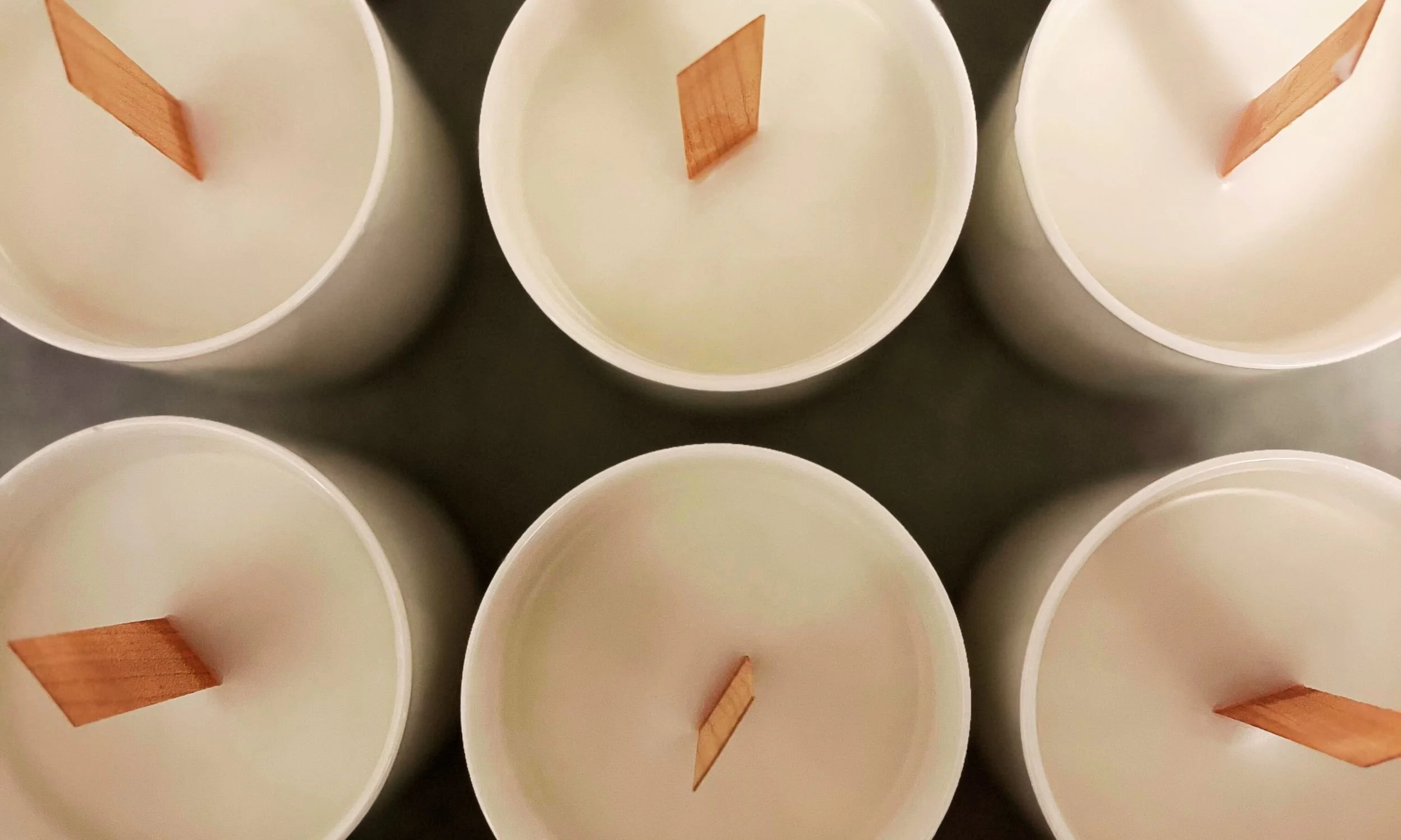 white candle vessels with smooth candle wax and wooden wicks