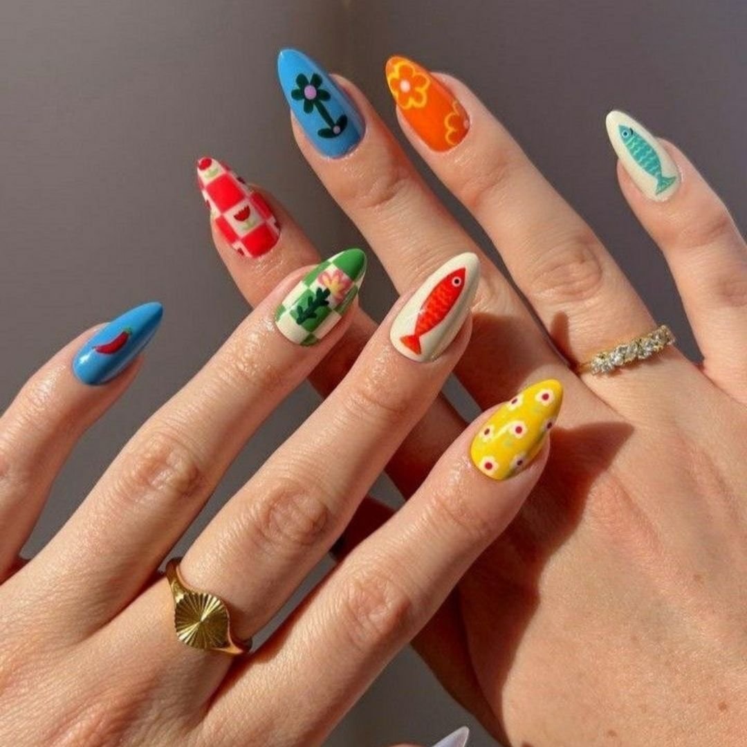 Colorful nails with beach and food-themed designs, including fish, ketchup, and a surfboard, on a person's fingers.