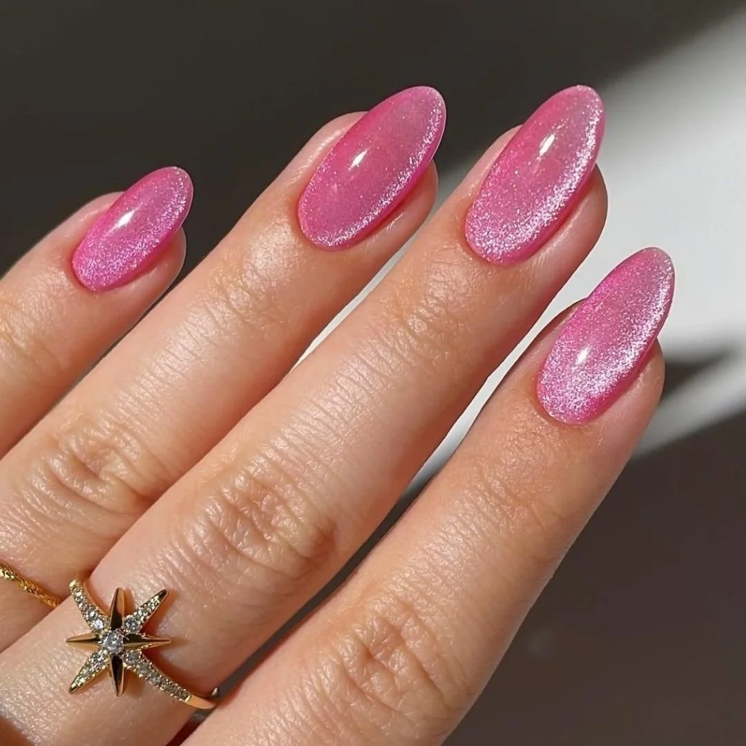 Close-up of a hand with pink, glittery, oval-shaped nail polish on fingernails and a gold ring with a star design and small diamonds.