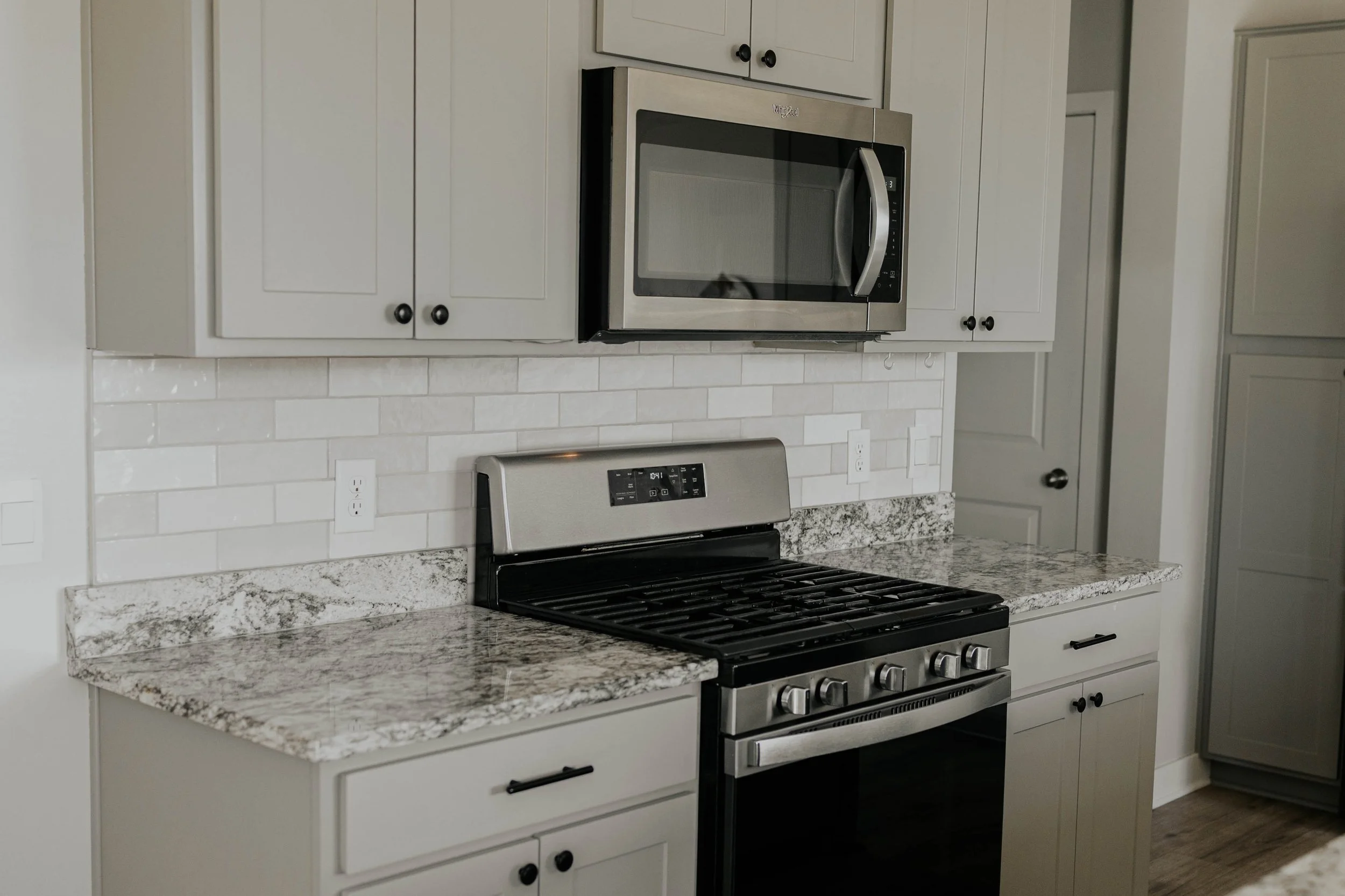 Modern kitchen with white cabinets, granite countertop, stainless steel microwave, and stove.