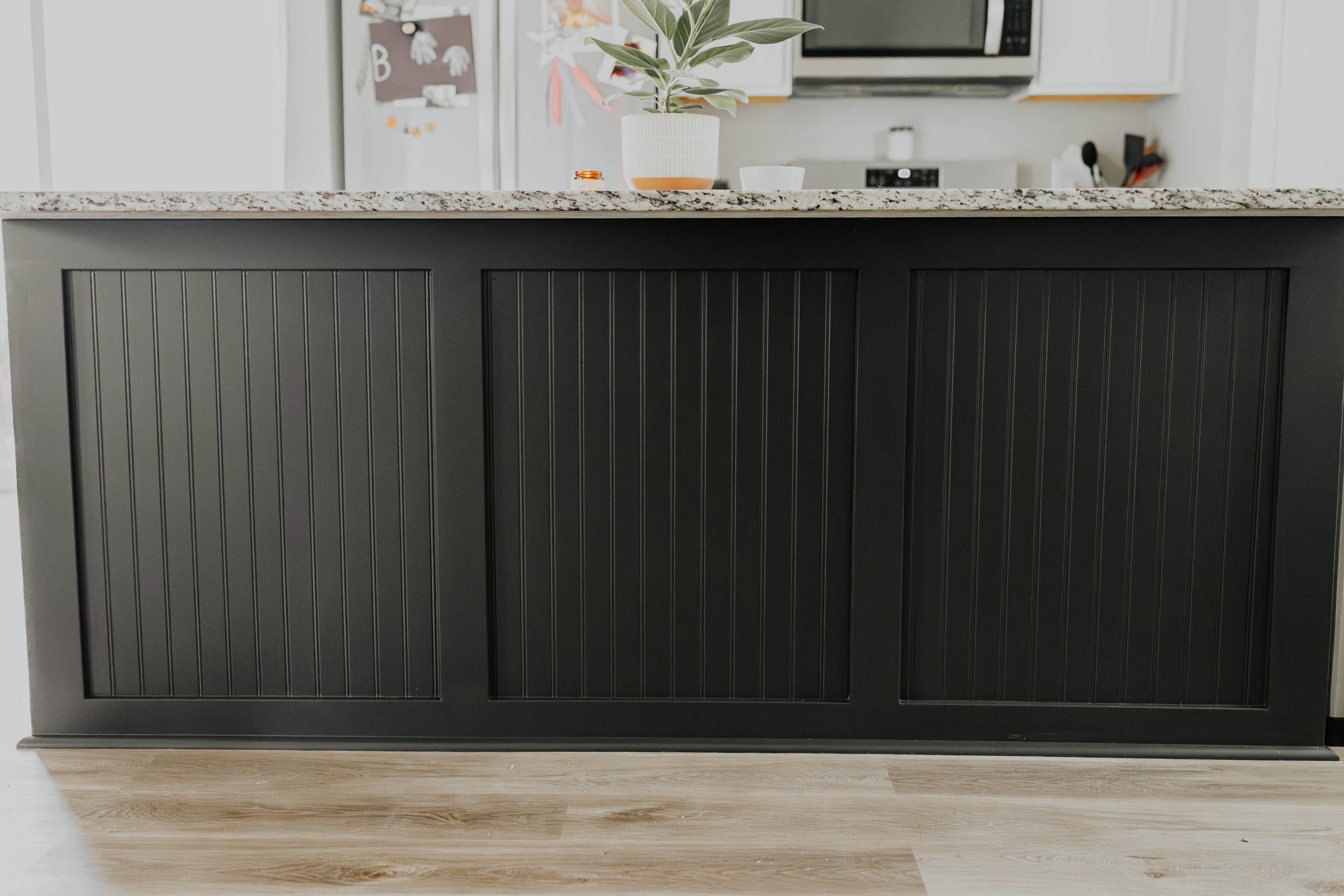 A kitchen island with dark paneling, a light-colored granite countertop, and a small potted plant on top.