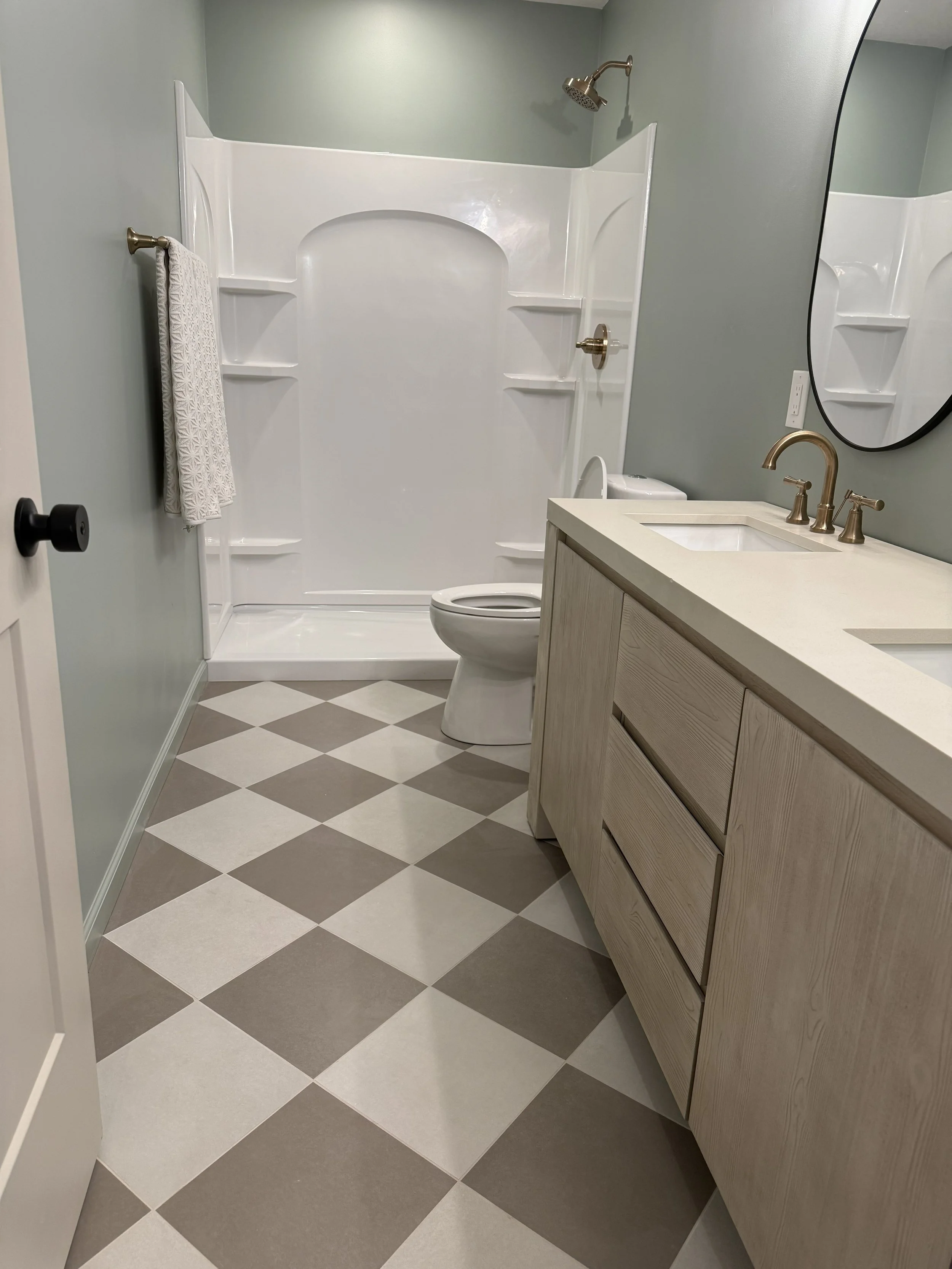 Full bathroom with white shower insert, champagne bronze fixtures, a light wood vanity and neutral checkerboard porcelain tile flooring