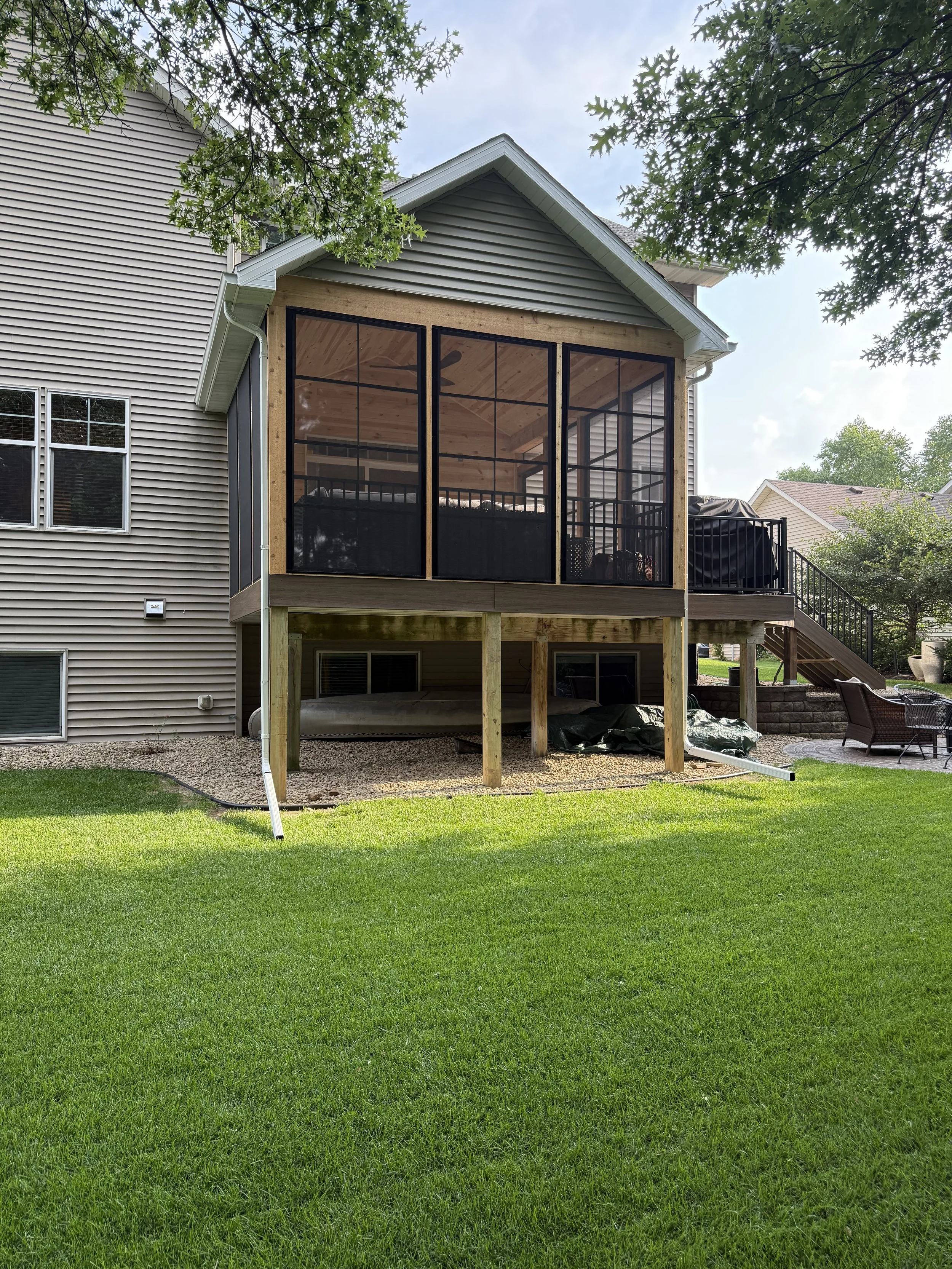 Backyard view of a house with a newly built screened porch on the upper level, with attached deck.