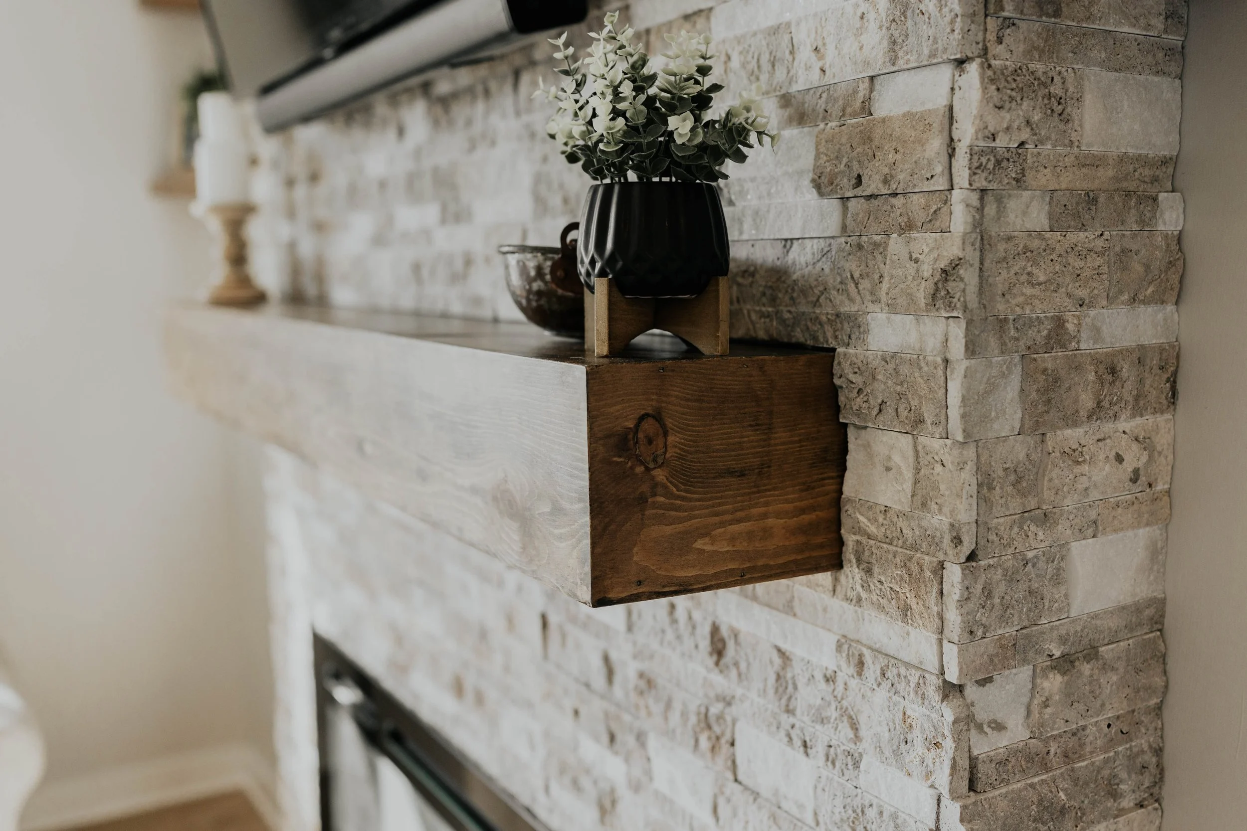 Close-up of a stone fireplace with a wooden mantel shelf decorated with a black vase with flowers and a candle holder.