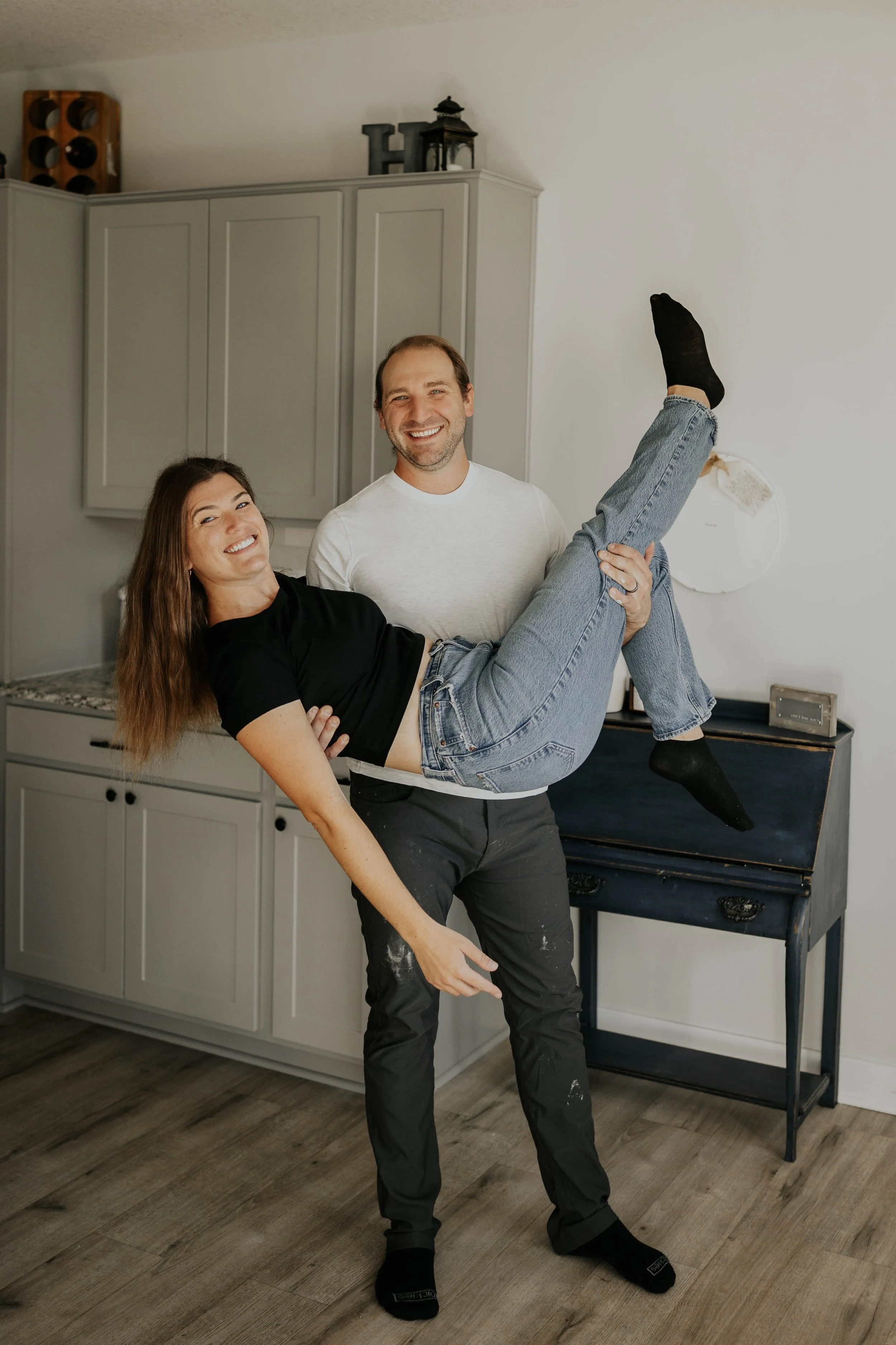 A man lifting a woman in a kitchen, both smiling.