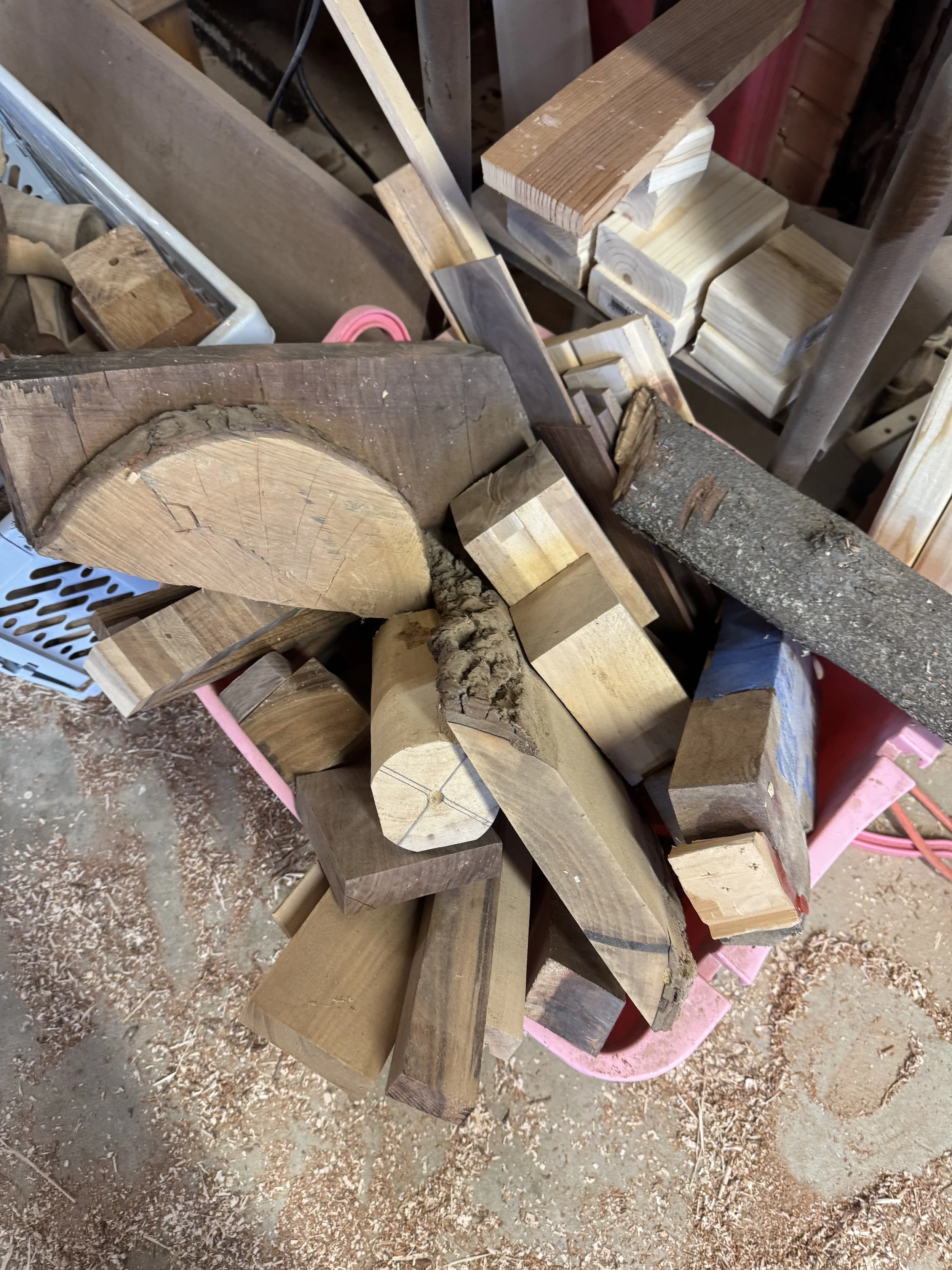 various pieces of cut and assembled wood in a workshop with sawdust on the floor.