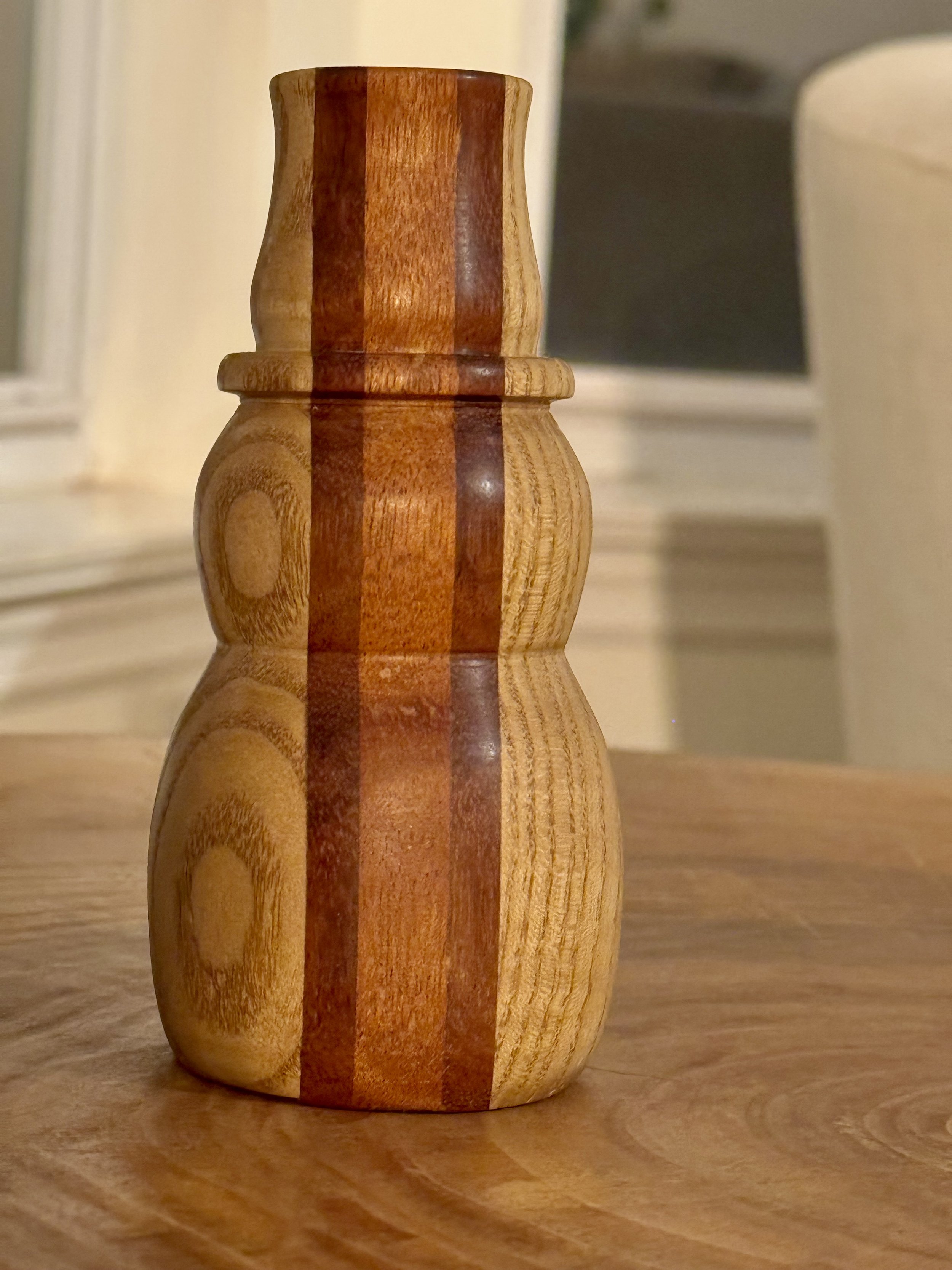 A wooden snowman with vertical dark and light wood stripes, sitting on a wooden surface.