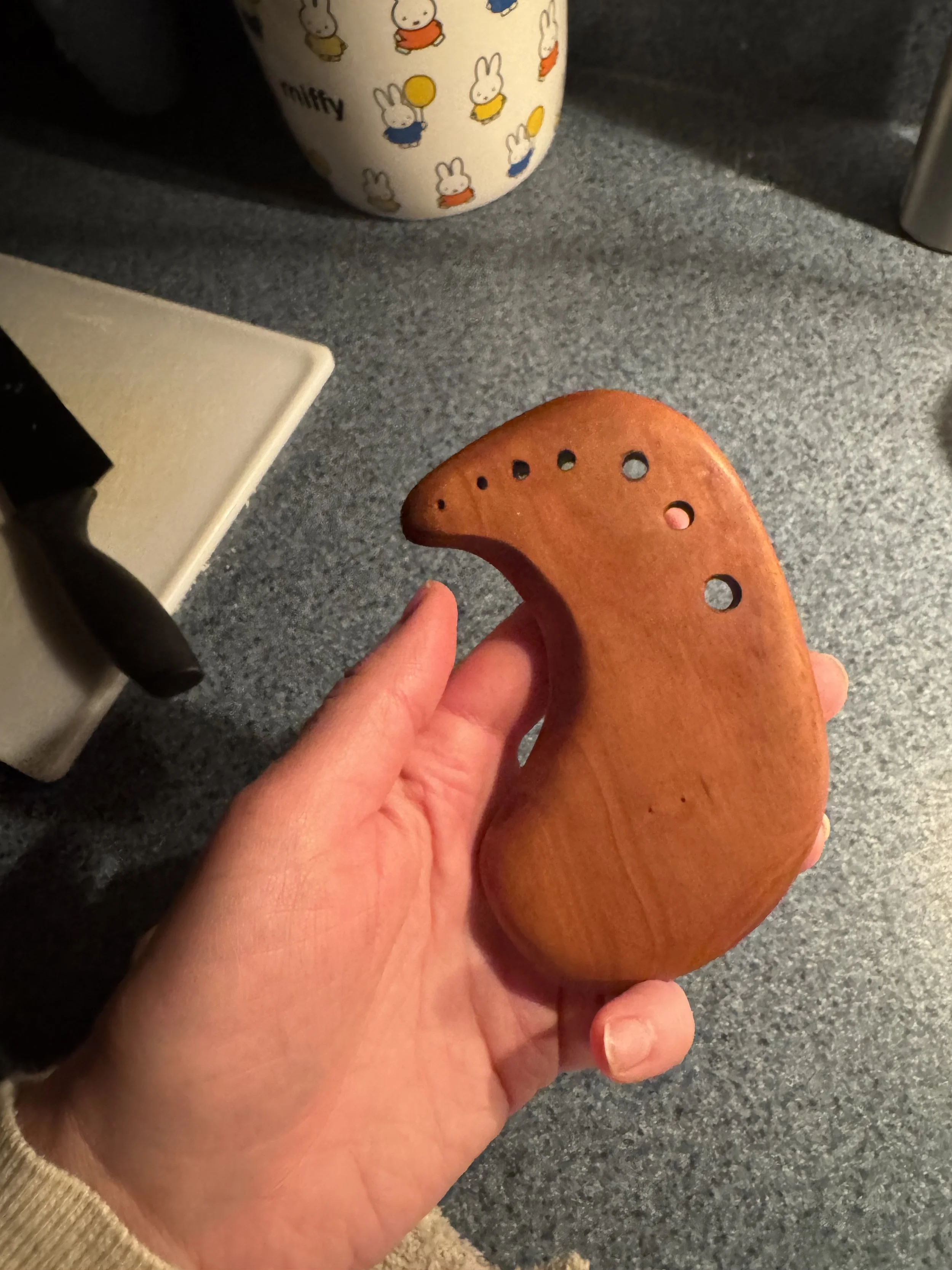 Hand holding a wooden herb stripper or herb puller, resting on a gray countertop in a kitchen.