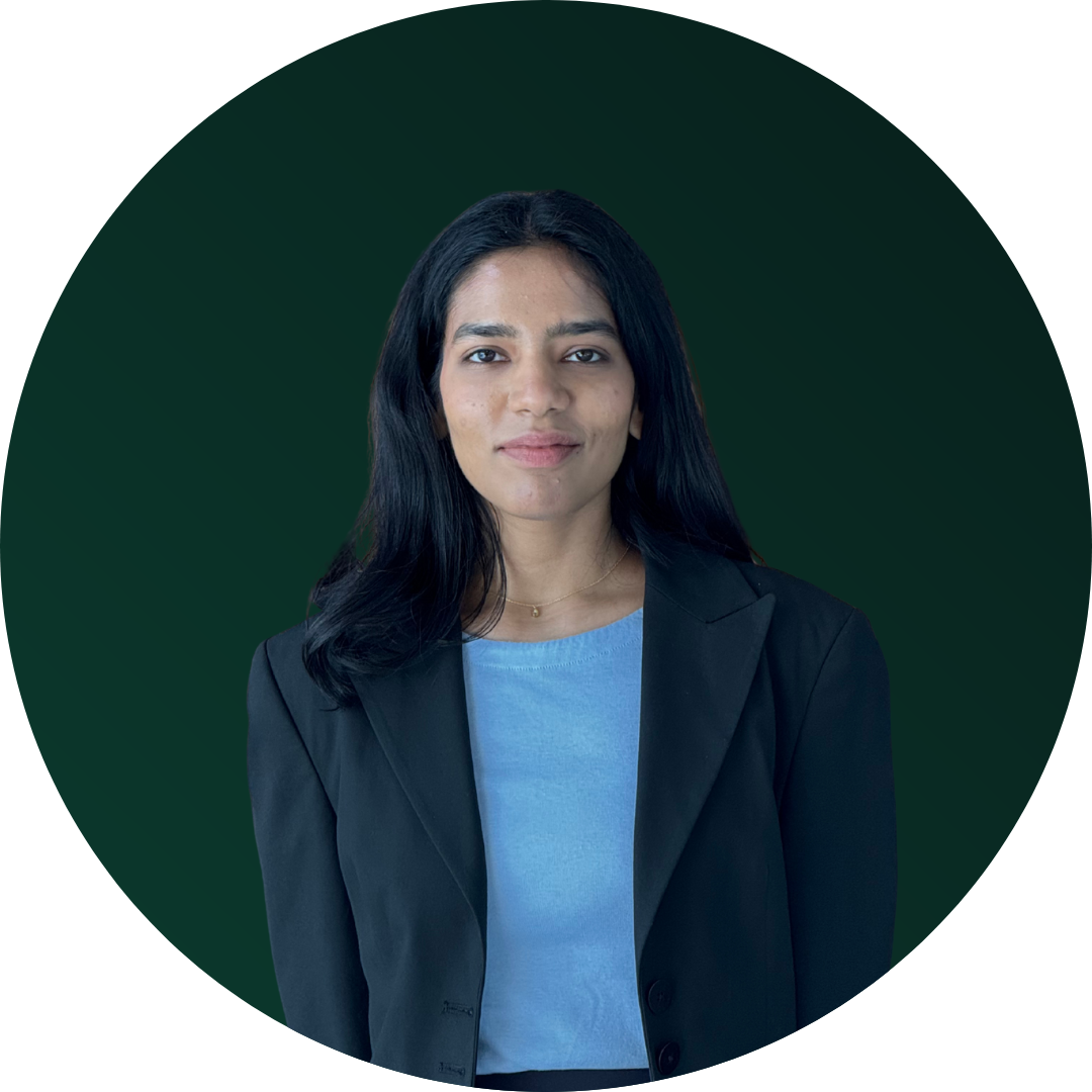 A woman with long black hair, wearing a black blazer over a light blue shirt, standing against a dark green circular background.