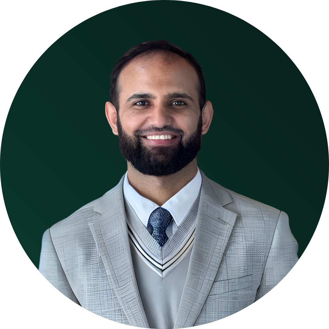 Headshot of a smiling man with a beard in a light grey suit, white shirt, and blue patterned tie, against a dark green background.