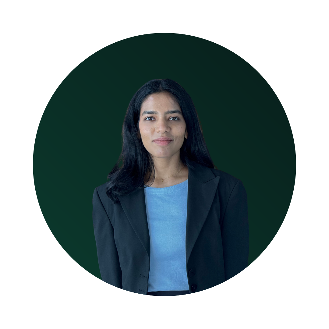 A woman with long black hair, wearing a black blazer over a light blue shirt, standing against a dark green circular background.