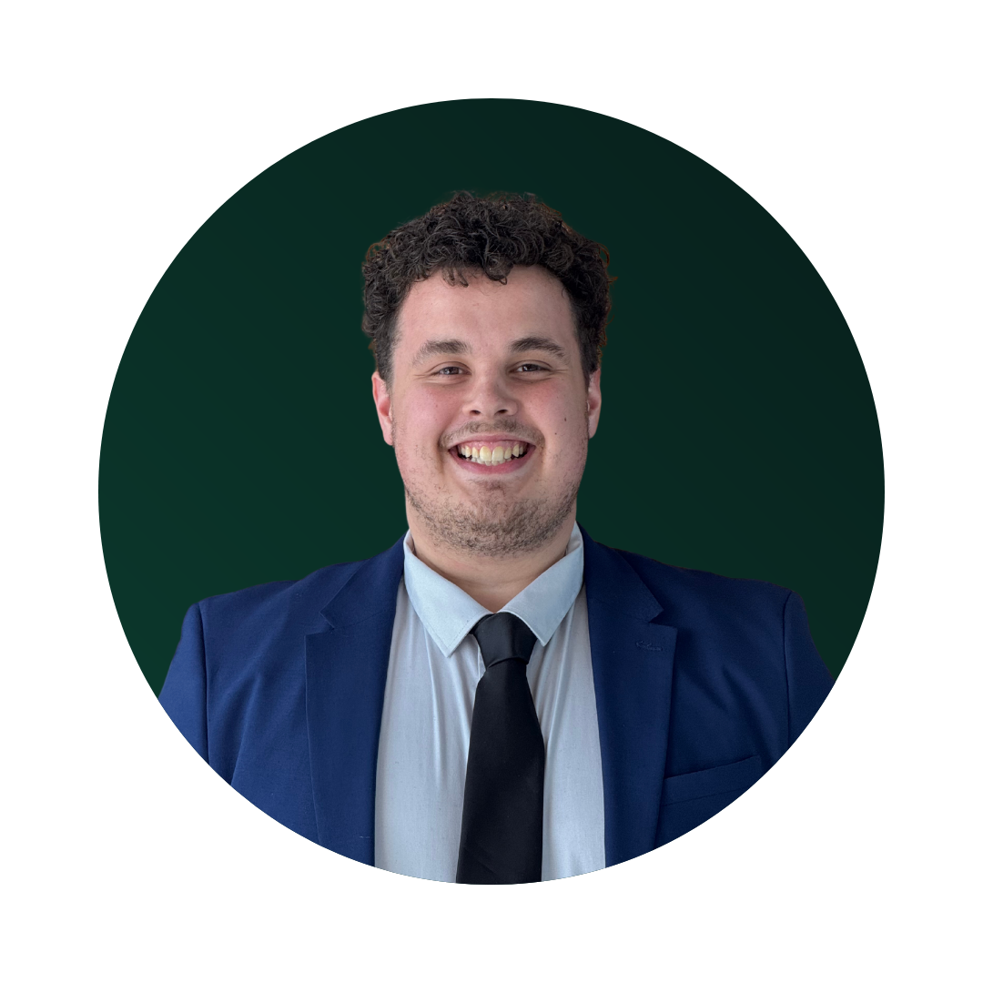 Portrait of a smiling man in a navy suit, light blue shirt, and black tie, with dark curly hair, in front of a dark green circular background.