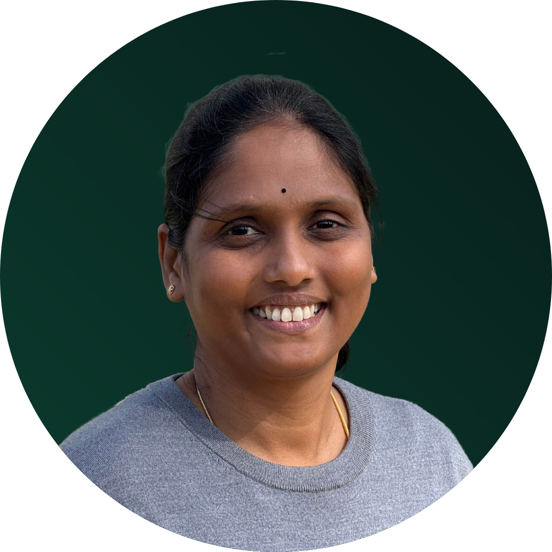A woman with dark hair, smiling, wearing a grey top and small earrings, against a dark green background.