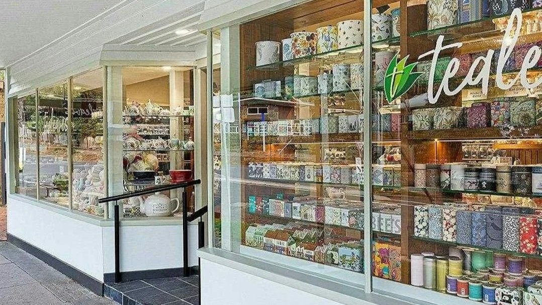 Display window of a store showing shelves filled with patterned gift wraps, sprinkles, and ceramic dishes.