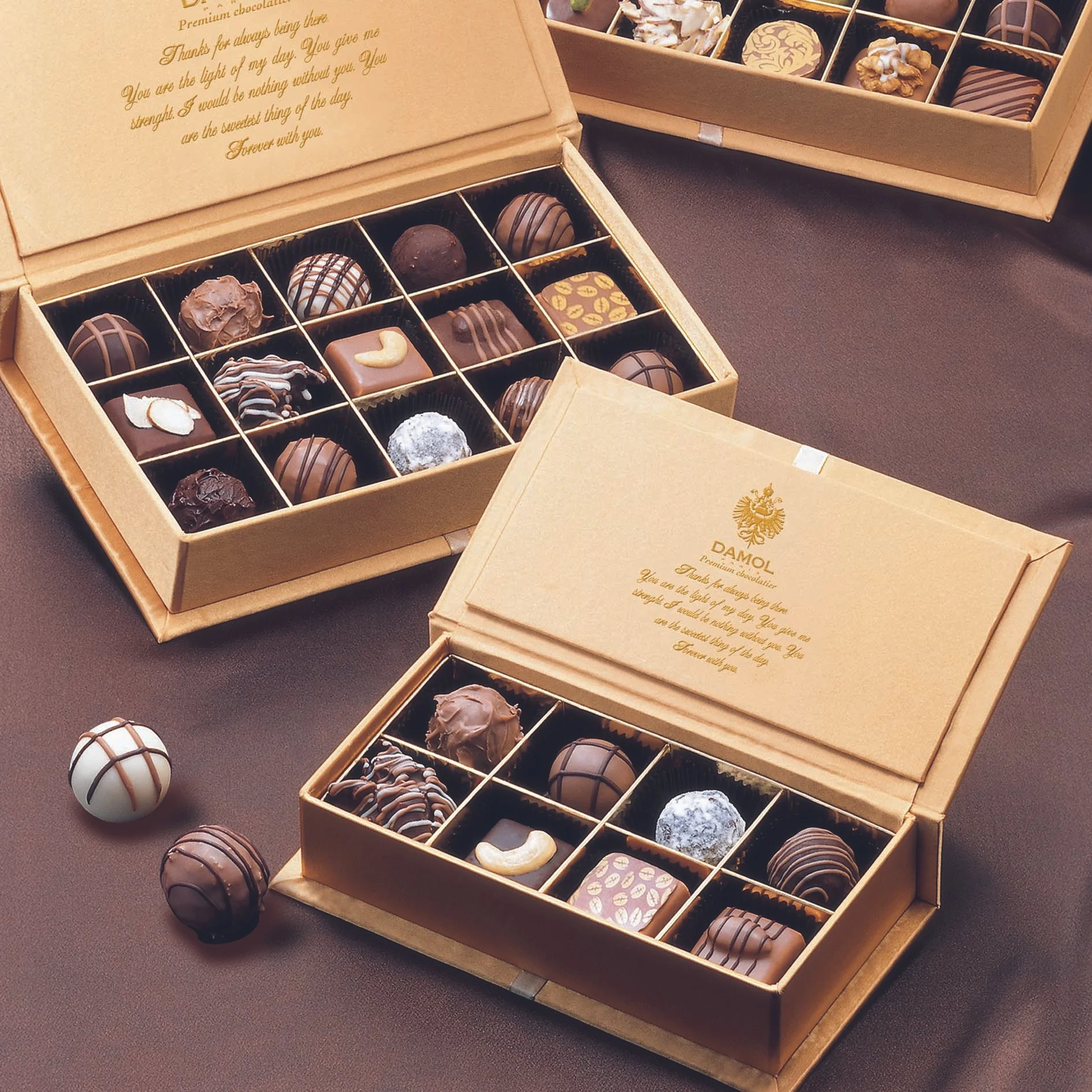 금색 패키지의 초콜릿 박스 두 개와 상자 밖에 놓인 다양한 수제 초콜릿이 갈색 표면 위에 놓인 모습