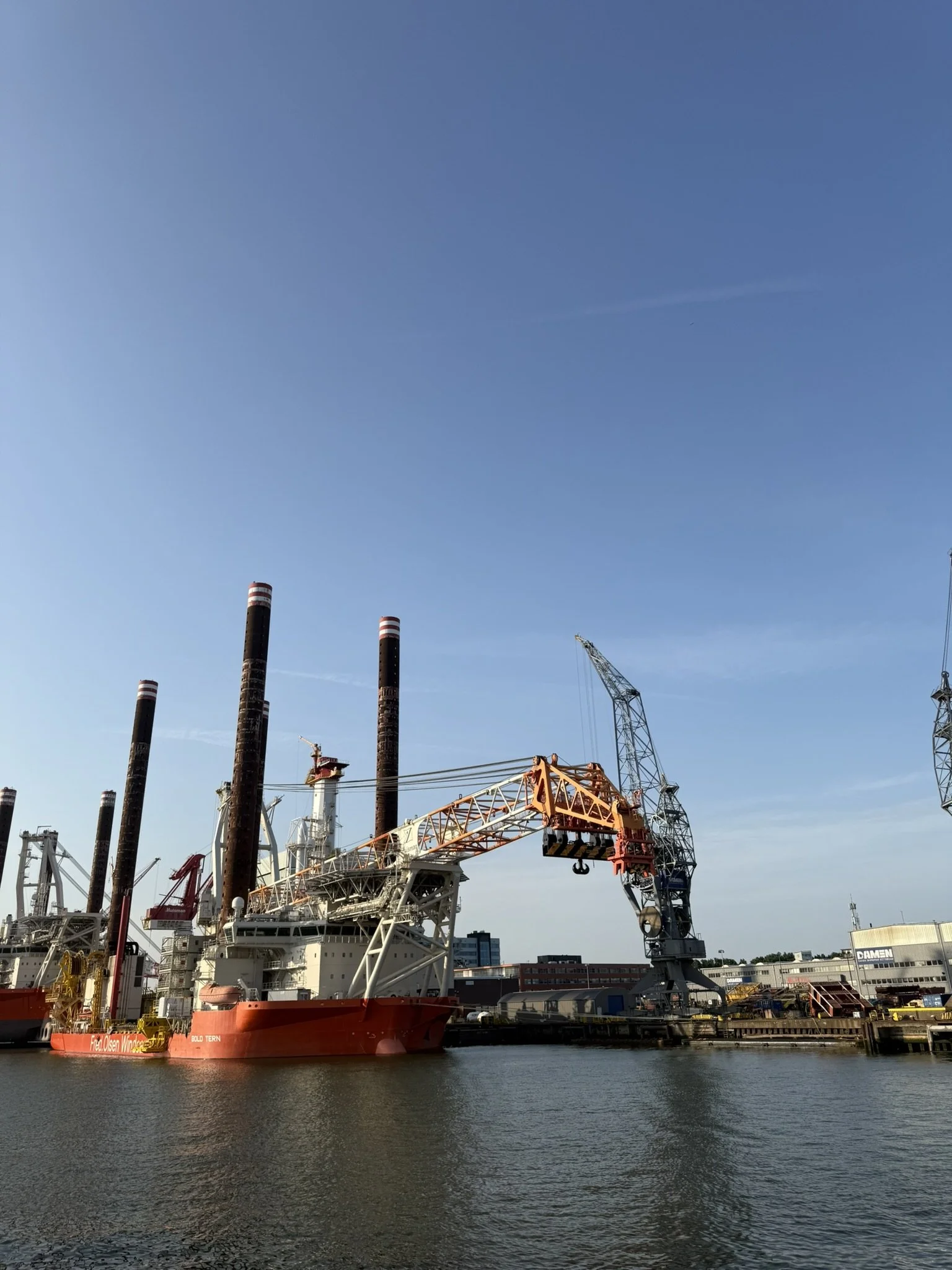 A young man with tattoos on his arm is sitting at a table and reading a piece of paper, possibly a medical document. A medical professional in blue scrubs and blue gloves is working at another table in the background.