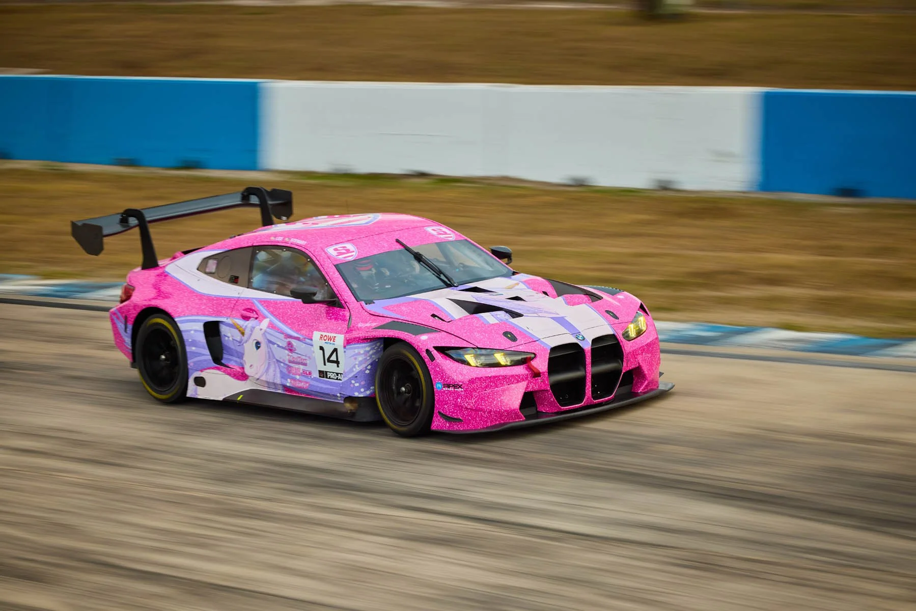 Pink race car with a unicorn graphic speeding on a racetrack.