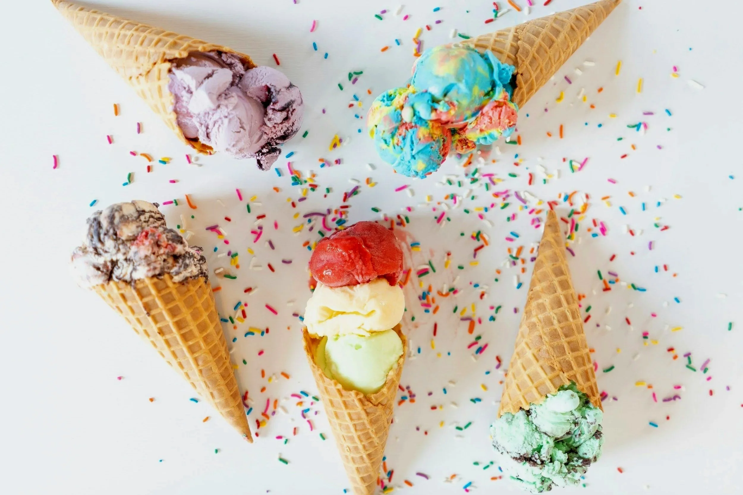 Five ice cream cones with different flavors, colorful sprinkles, and a white background.