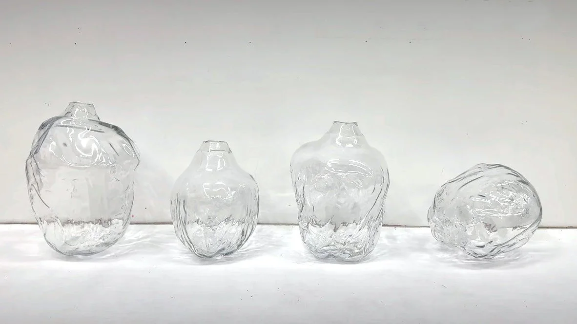Four irregularly shaped clear glass vases or sculptures, displayed on a white surface against a plain white background.