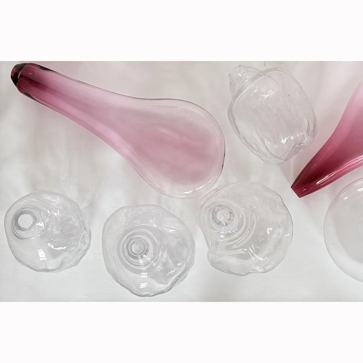 Collection of pink and clear glass vases and bowls on a white surface.