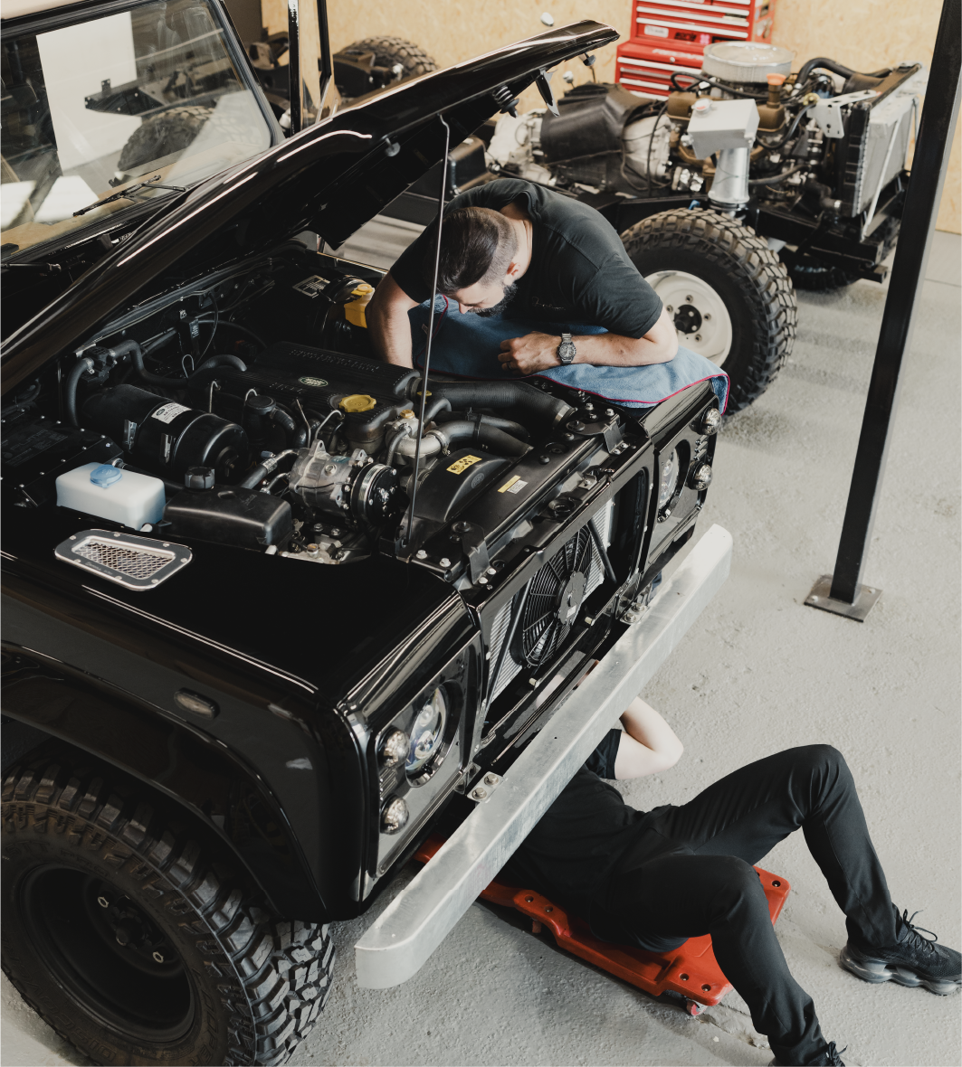 Shoreline technician working under the bonnet of a black Land Rover Defender in the workshop