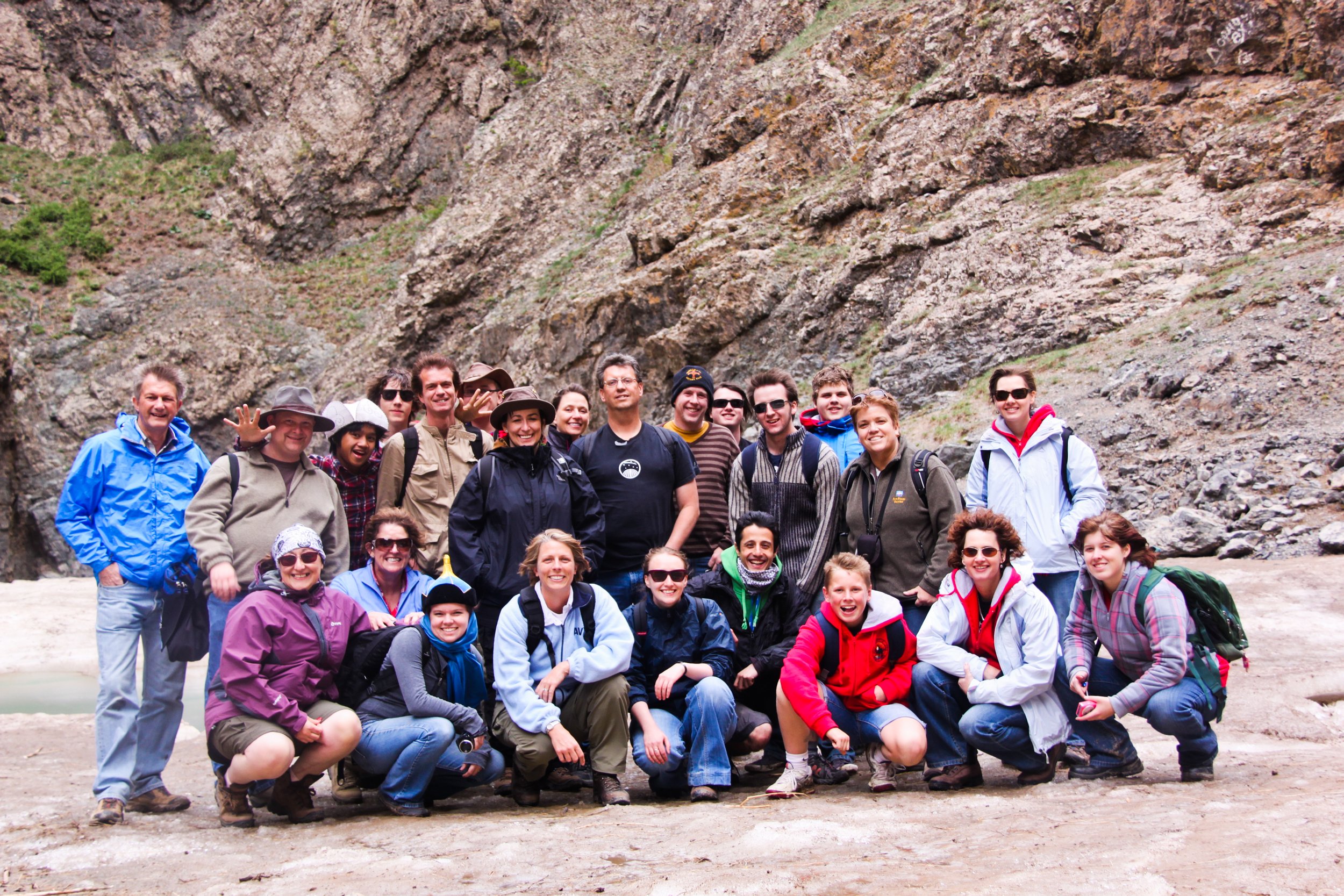 A group of people smiling and posing for a photo outdoors in a rocky canyon or mountain area, dressed in casual and outdoor clothing.