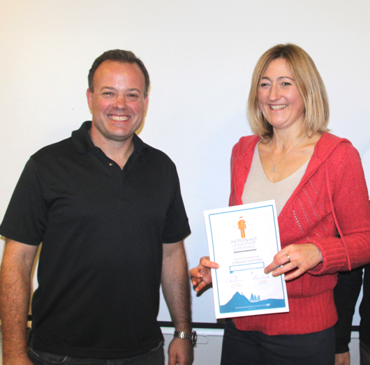 A man and a woman smiling, with the woman holding a certificate of achievement.
