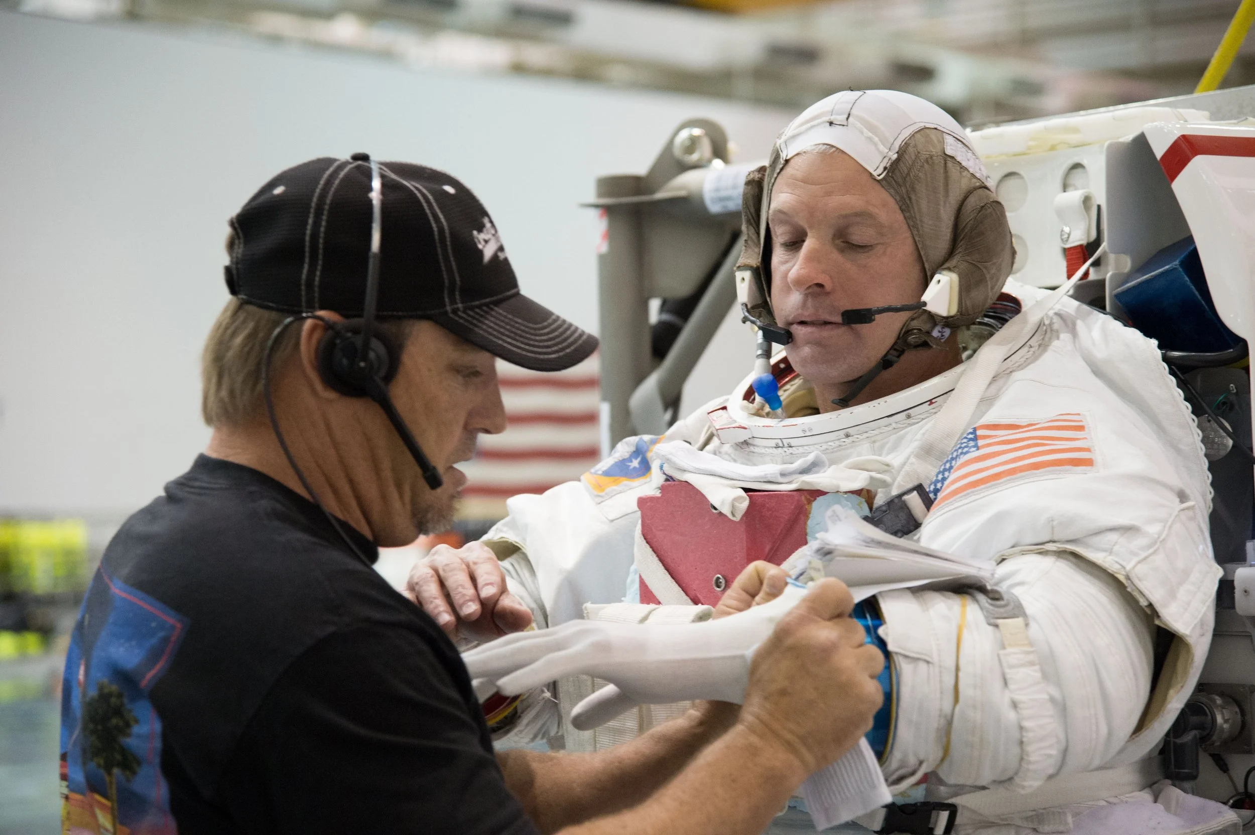 Astronaut being attended to by medical personnel while in a space suit inside a facility.