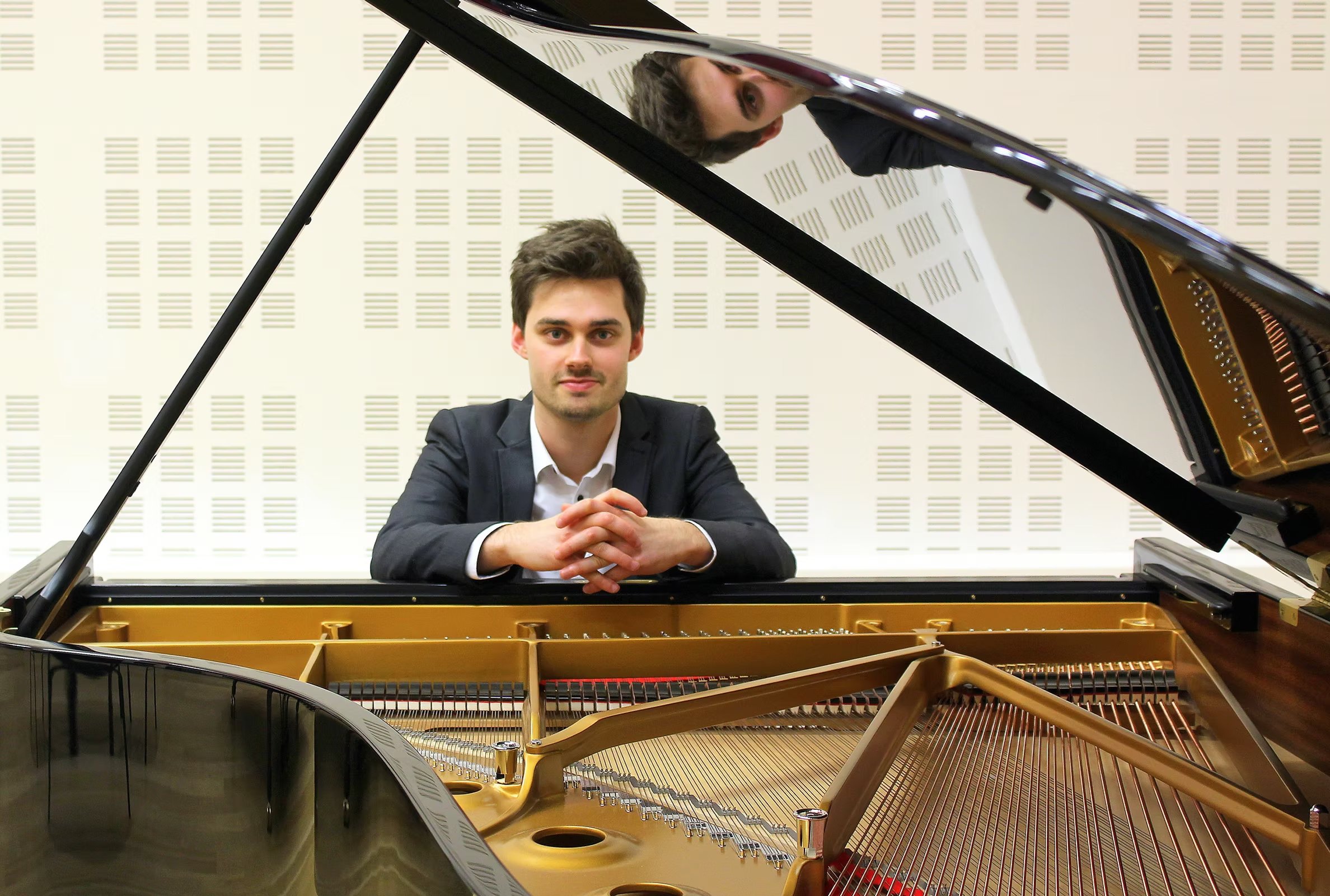 A man sitting at a grand piano, looking at the camera, with the lid of the piano open.