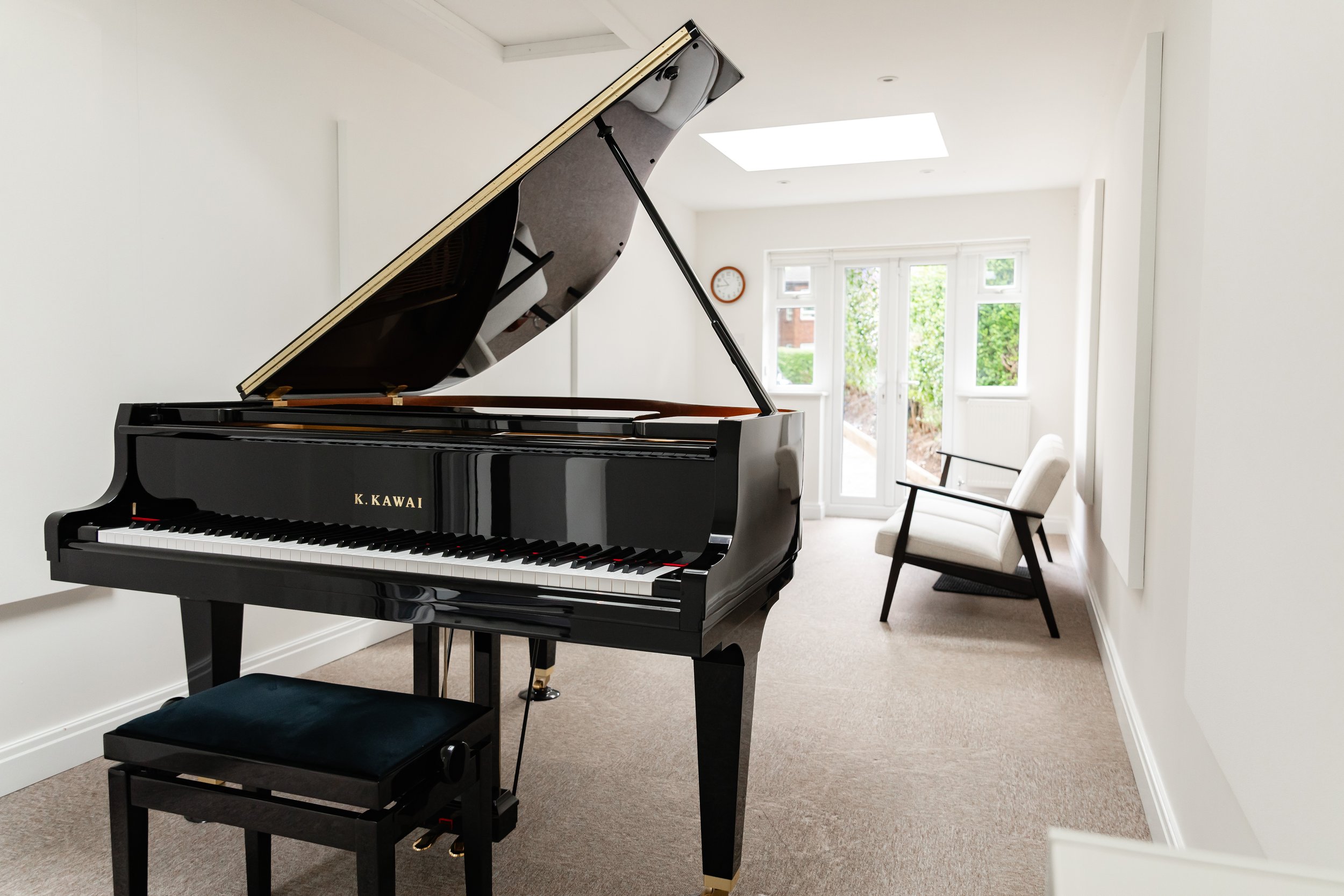 A Virtuoso Project live session room with a black grand piano with gold lettering in a bright, minimalist room.