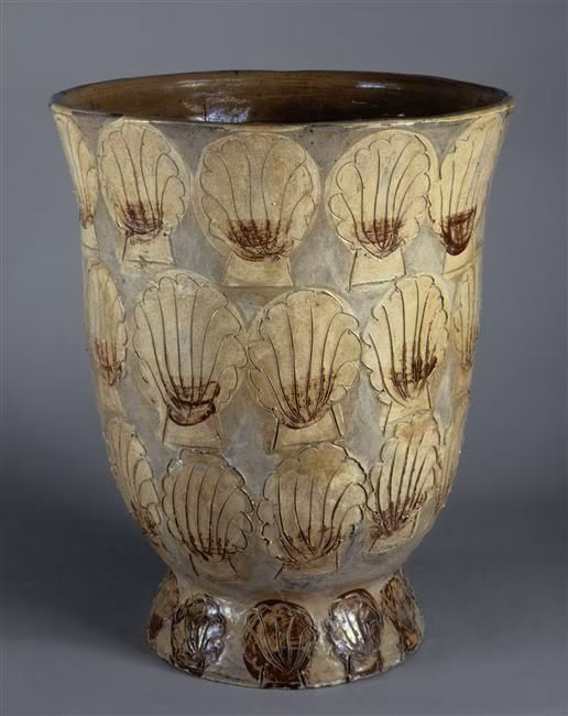 Ancient pottery vessel decorated with shell motifs and stylized shells in beige, brown, and cream colors.
