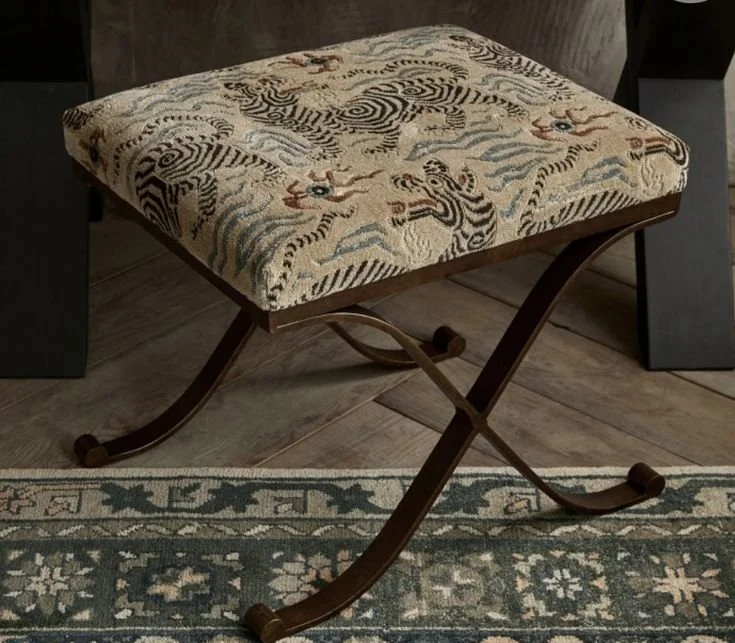 A black iron french style benhc with a beautiful uphostered seat featuring a tiger and wave pattern upholstery, placed on a patterned rug in a room.