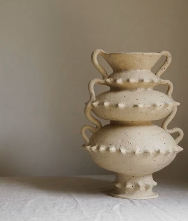 A stack of four cream-colored, textured ceramic vases with handles on each side, arranged from largest at the bottom to smallest at the top, set against a neutral background.