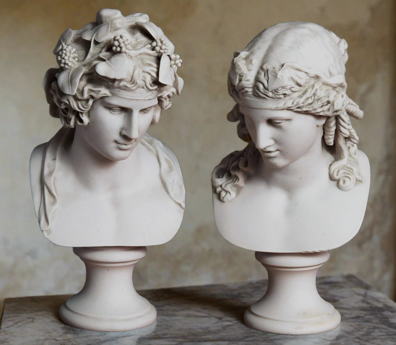 Two marble bust sculptures of a man and a woman with detailed hair, placed on pedestals on a marble surface.