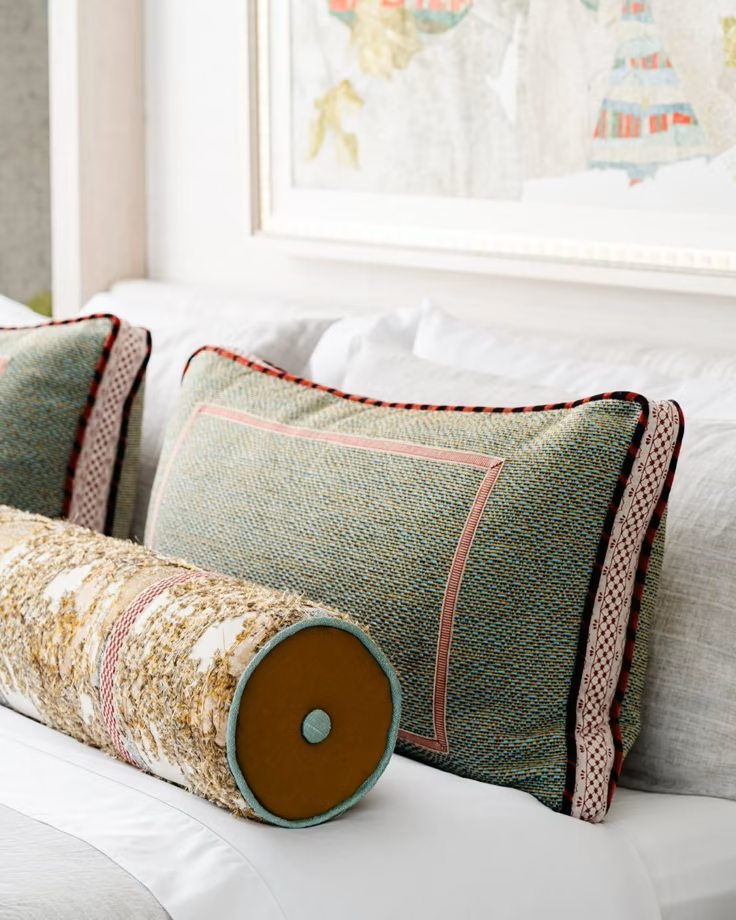 Decorative pillows and bolster on a bed with a framed picture or map on the wall in the background.