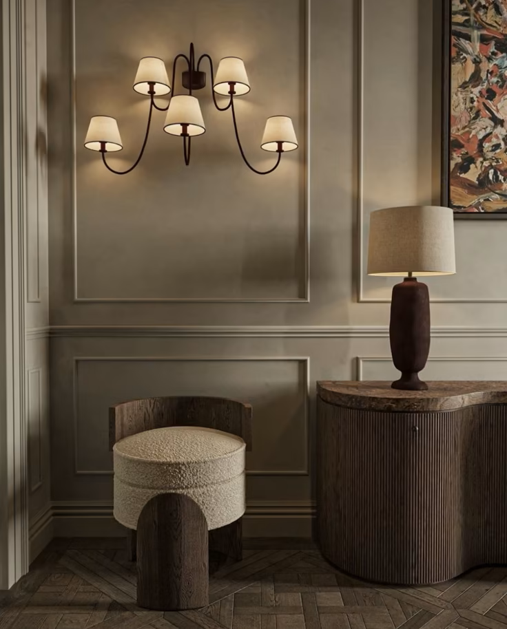 Interior corner with a wall-mounted chandelier, a side table with a table lamp, and a round chair, in a modern classic style.