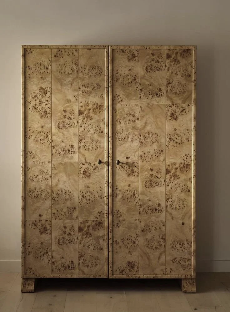 An antique wardrobe with panel doors, featuring a unique burl wood pattern, positioned against a plain wall.