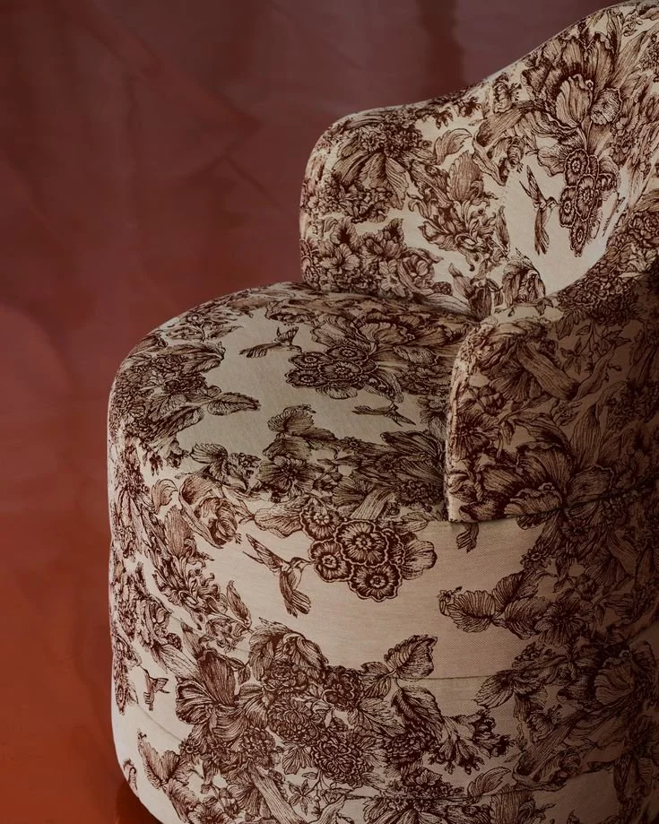 Close-up of a floral patterned armchair with a matching cushion, placed on a wooden floor.
