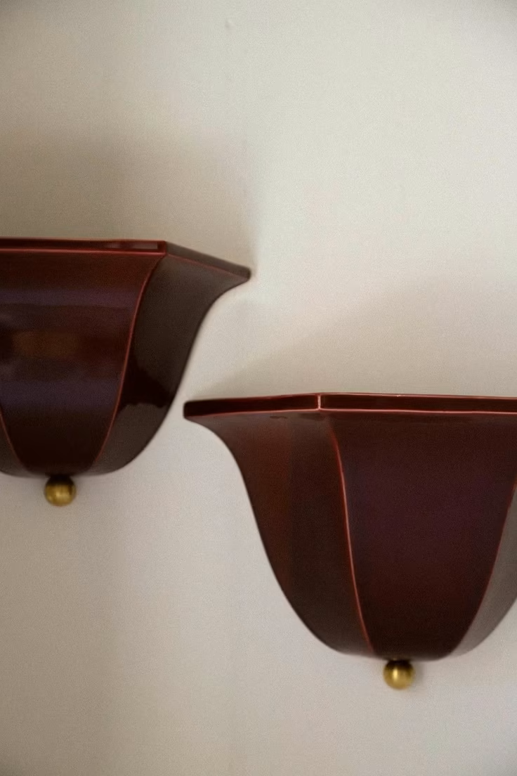 Two tulip shaped ceramic wall sconces in a dark reddish-brown colour, gold-colored balls at the bottom, mounted on a white wall.