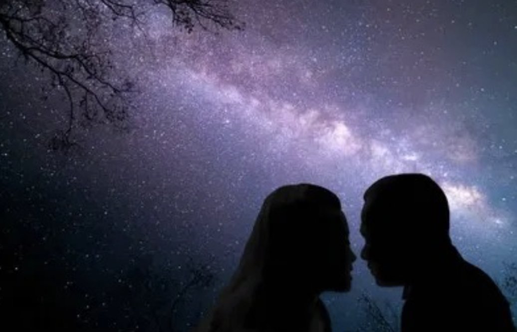 Silhouettes of a couple facing each other at night under a starry sky with the Milky Way galaxy visible in the background.